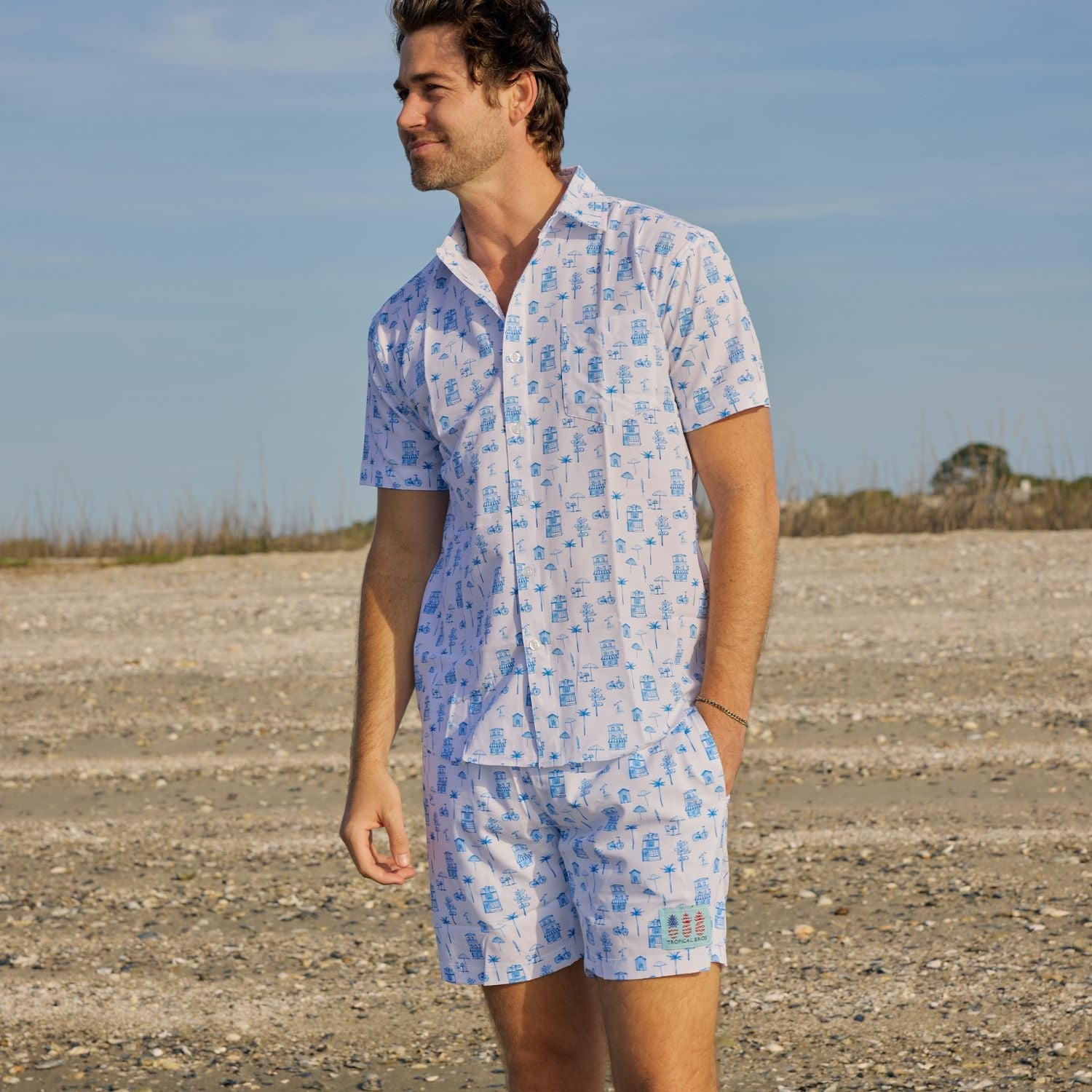 Man wearing a blue and white patterned shirt and shorts set standing in an open field.