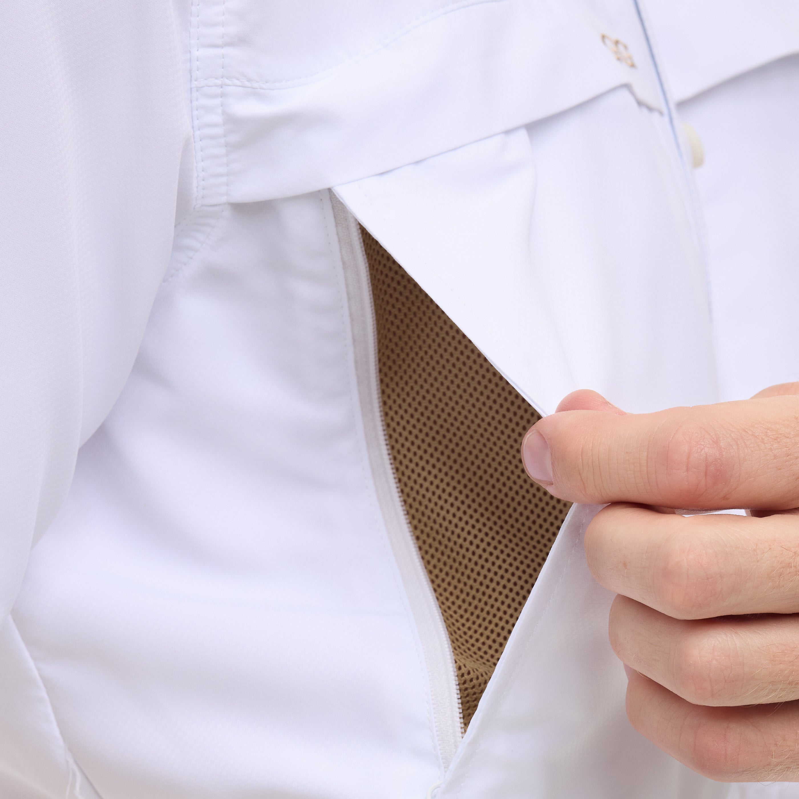 Close-up of a white shirt with a brown pocket detail, held open by a hand.
