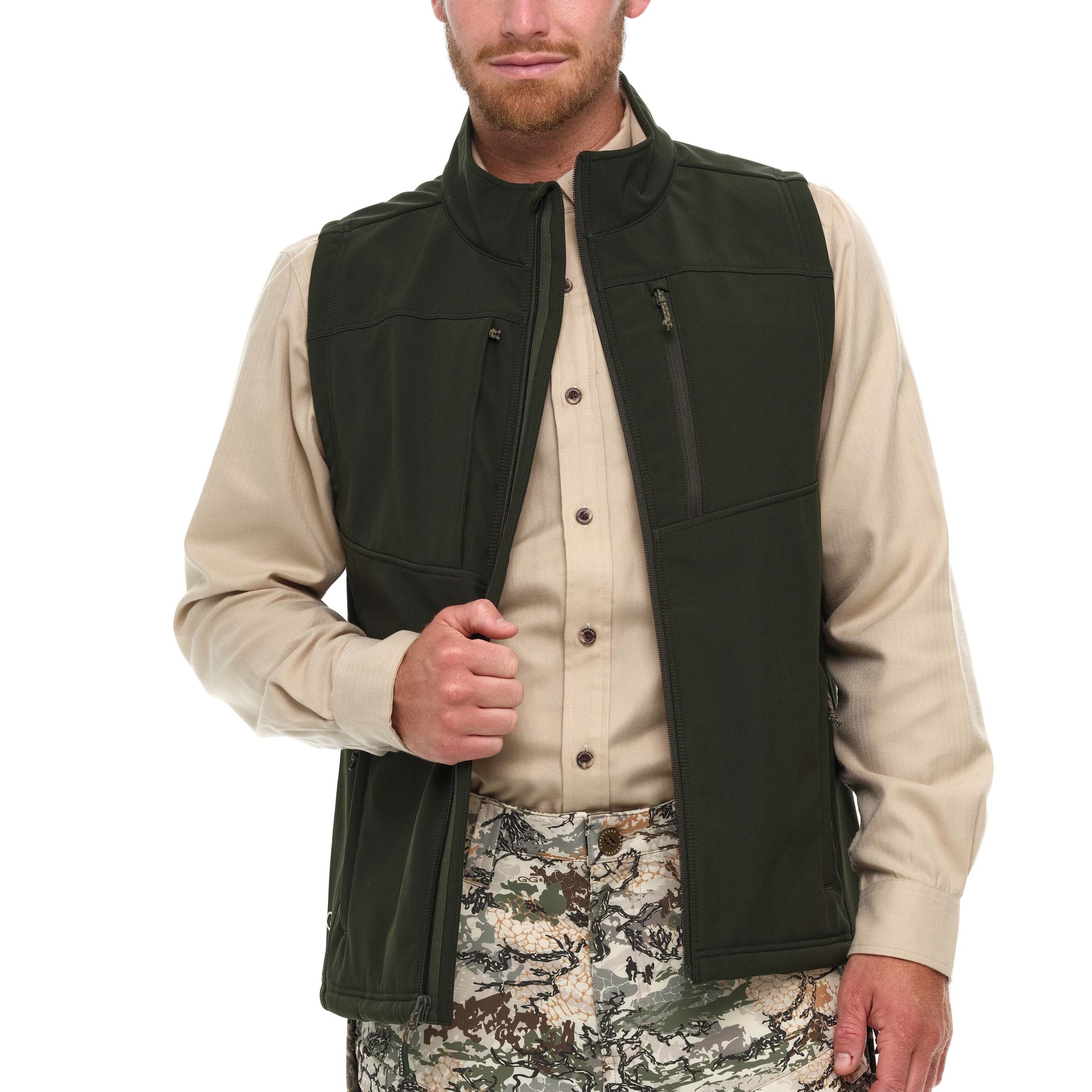 Man wearing a green vest over a beige shirt with camouflage pants on a white background