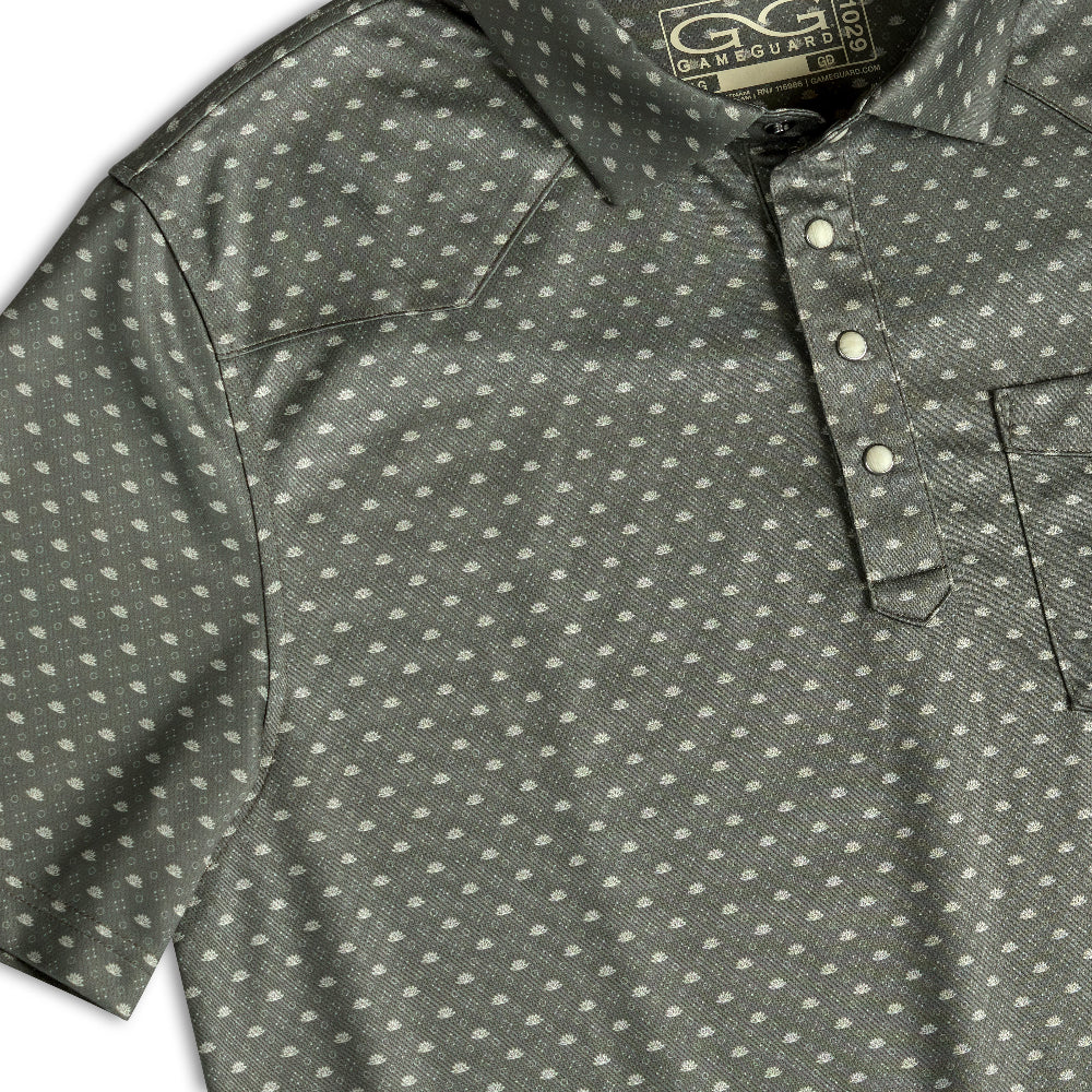 Close-up of a short-sleeve collared polo shirt with a repeating small white dot pattern on a dark gray base. The shirt has a three-button placket and a chest pocket, with a visible neck label reading GAYGUARANTEED.