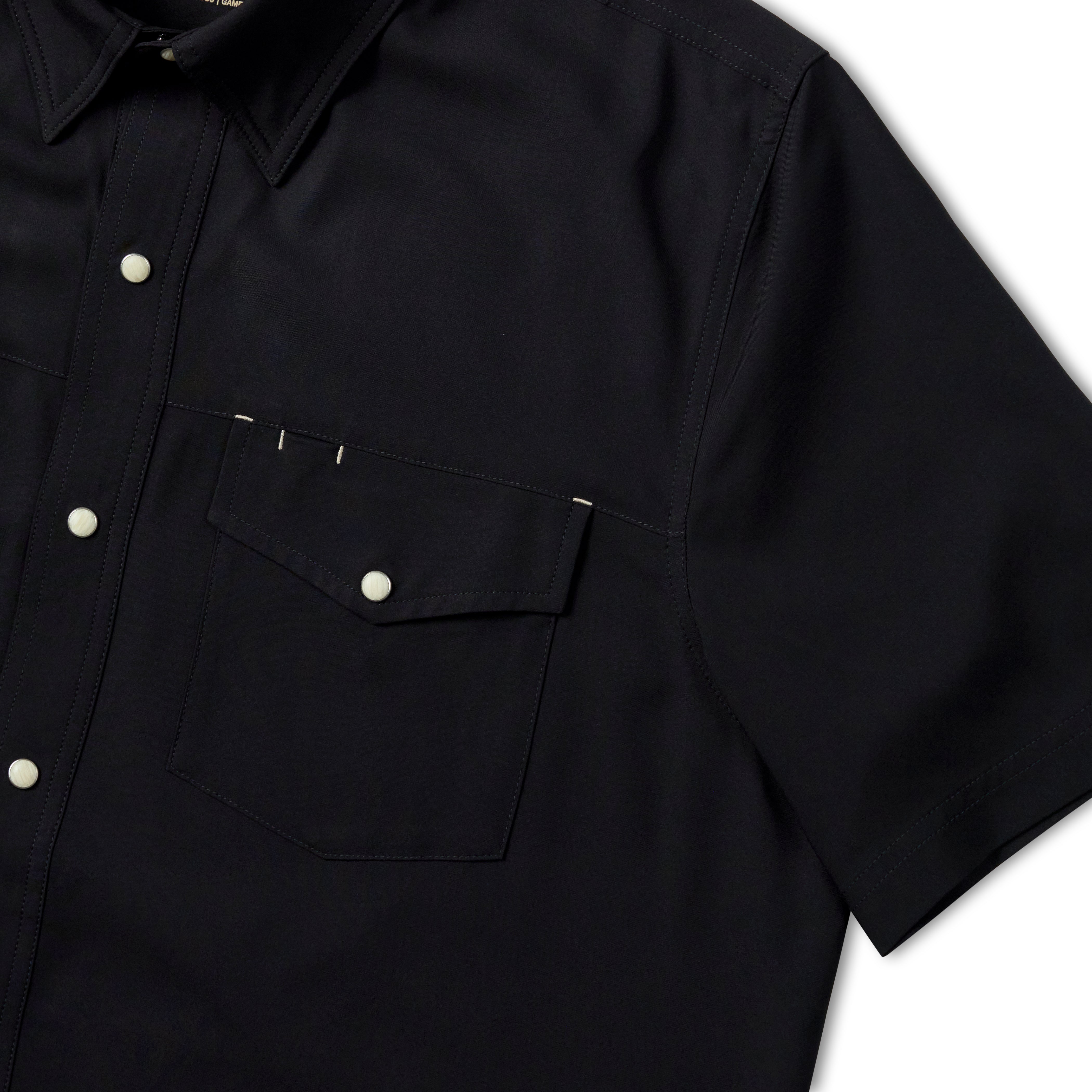 Close-up of a black short-sleeve button-up shirt with a chest pocket and silver snap buttons, shown against a dark background.