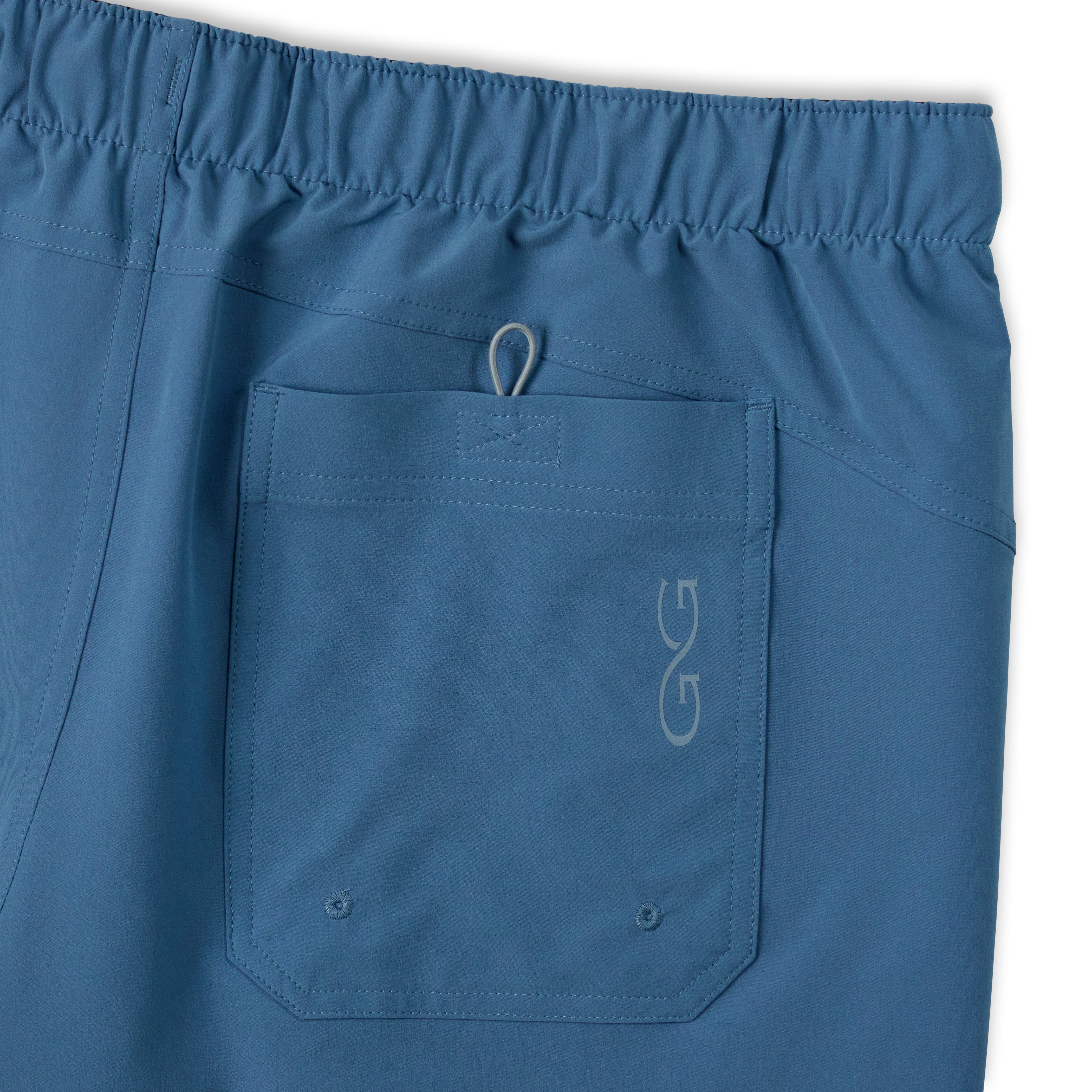 Close-up of blue scrub pants showing an elastic waistband and a front pocket with a small white embroidered logo.