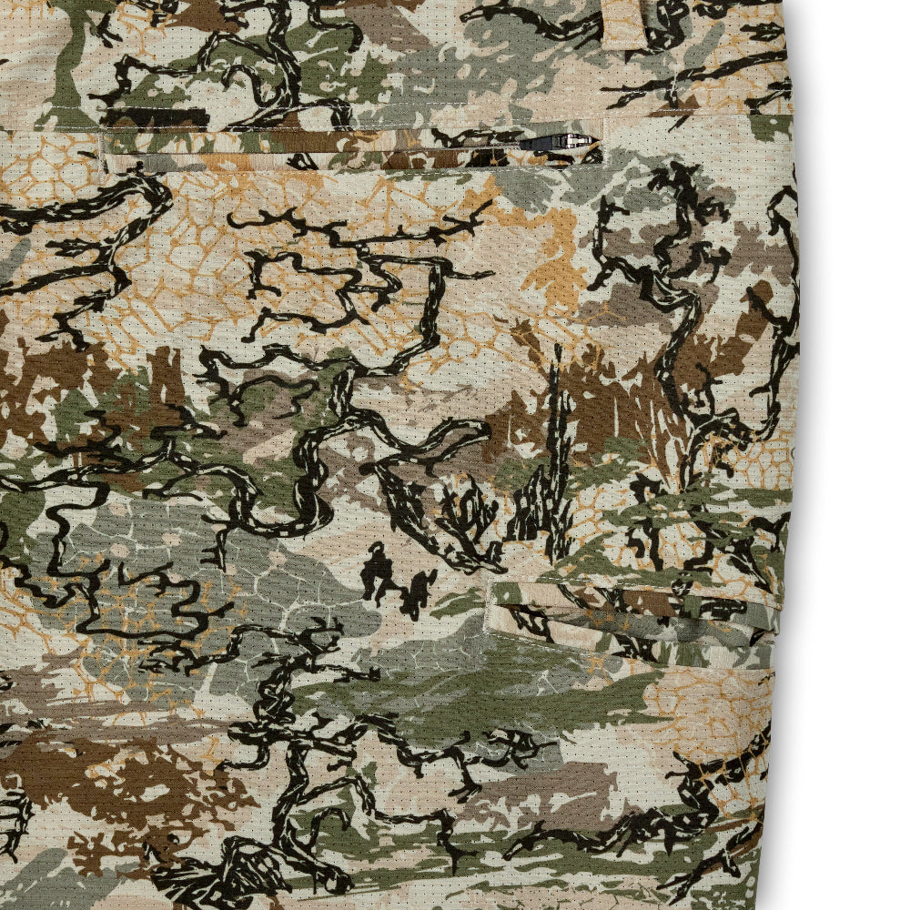 Close-up of a camouflage fabric pattern with irregular patches of beige, brown, green, and black outlined shapes.