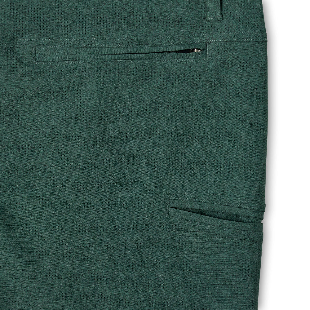 Close-up of dark green textured trousers showing a side pocket with a zipper and another side pocket, set against a plain white background.