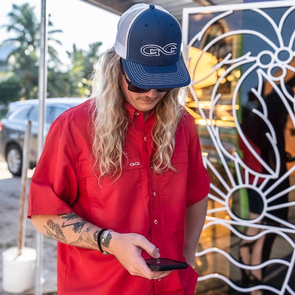 Person wearing a red shirt and blue cap with a logo, standing outdoors.