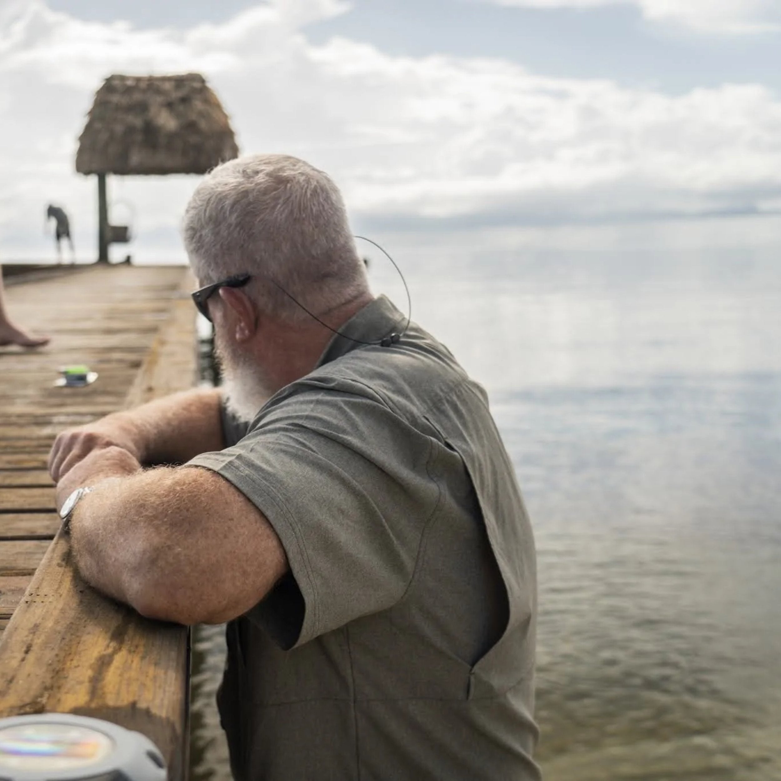 Man sitting on a wooden pier by the water, looking out over the water.