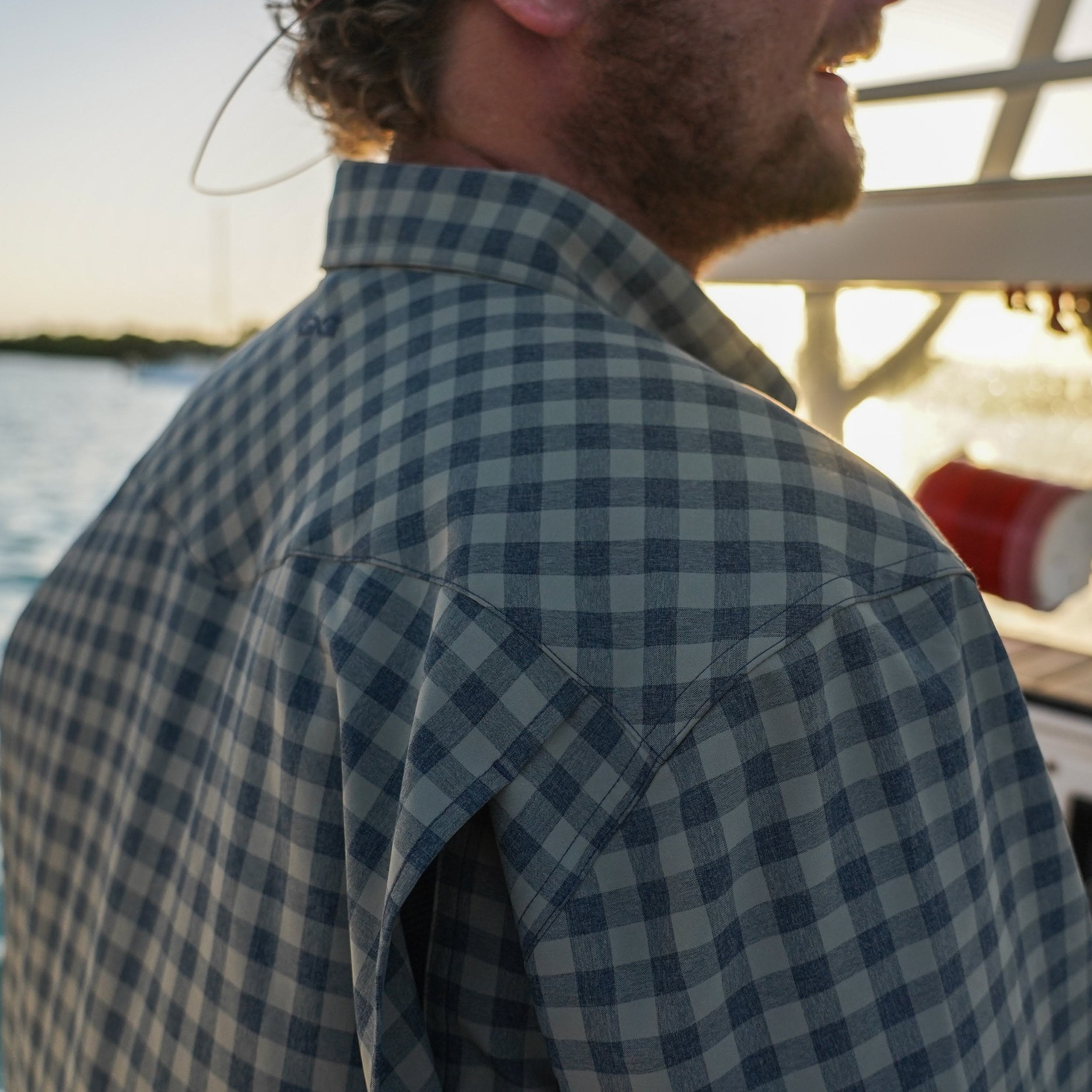 Man wearing a blue and green checkered shirt by a body of water.