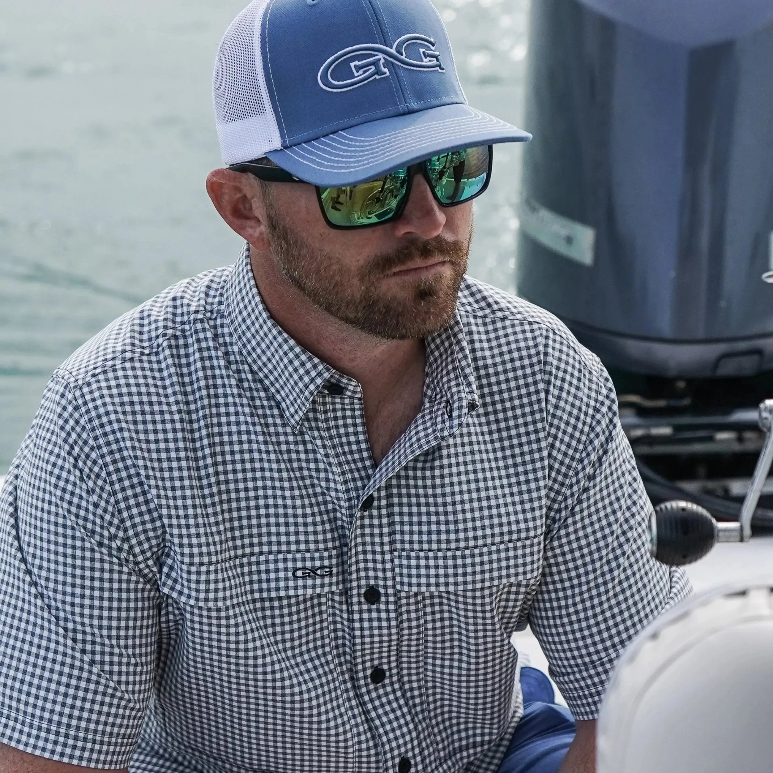 Man wearing a blue cap and sunglasses, sitting on a boat.