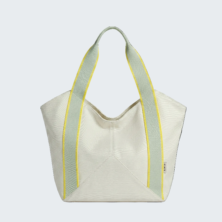 An off-white structured tote bag with pale green shoulder straps outlined in bright yellow piping, shown against a plain white background.