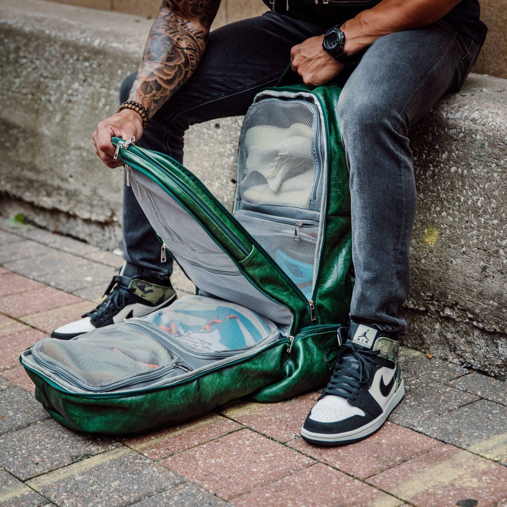 Person sitting on a step with an open green bag containing items on a sidewalk.