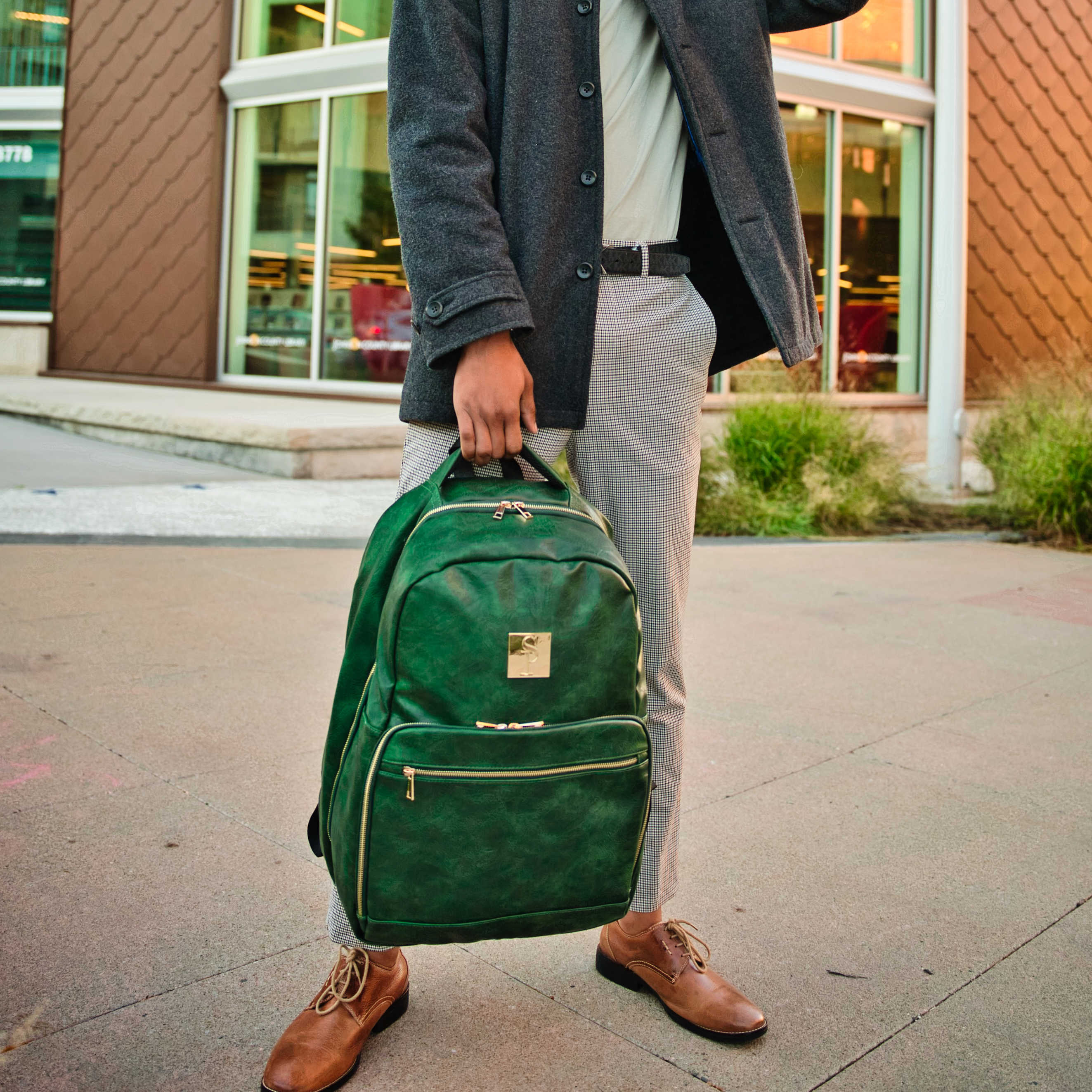 Person holding a green backpack on a sidewalk