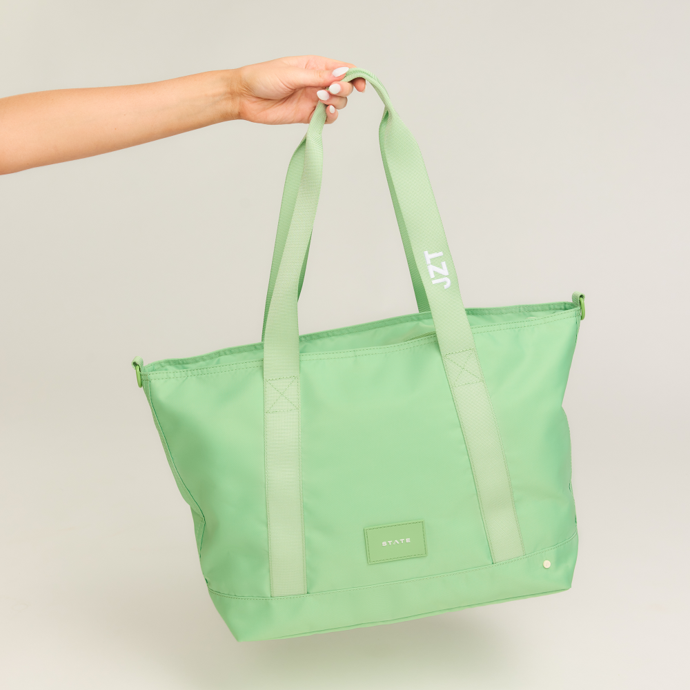 Green tote bag held by a hand against a light gray background