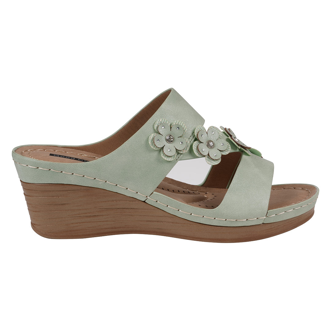 Light green sandal with wooden wedge sole and floral embellishments on a white background