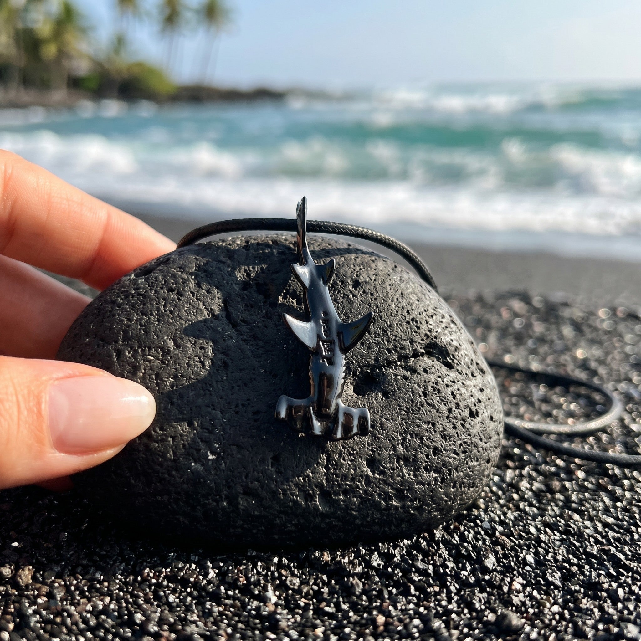Small shark figurine on a black stone with ocean and beach in the background