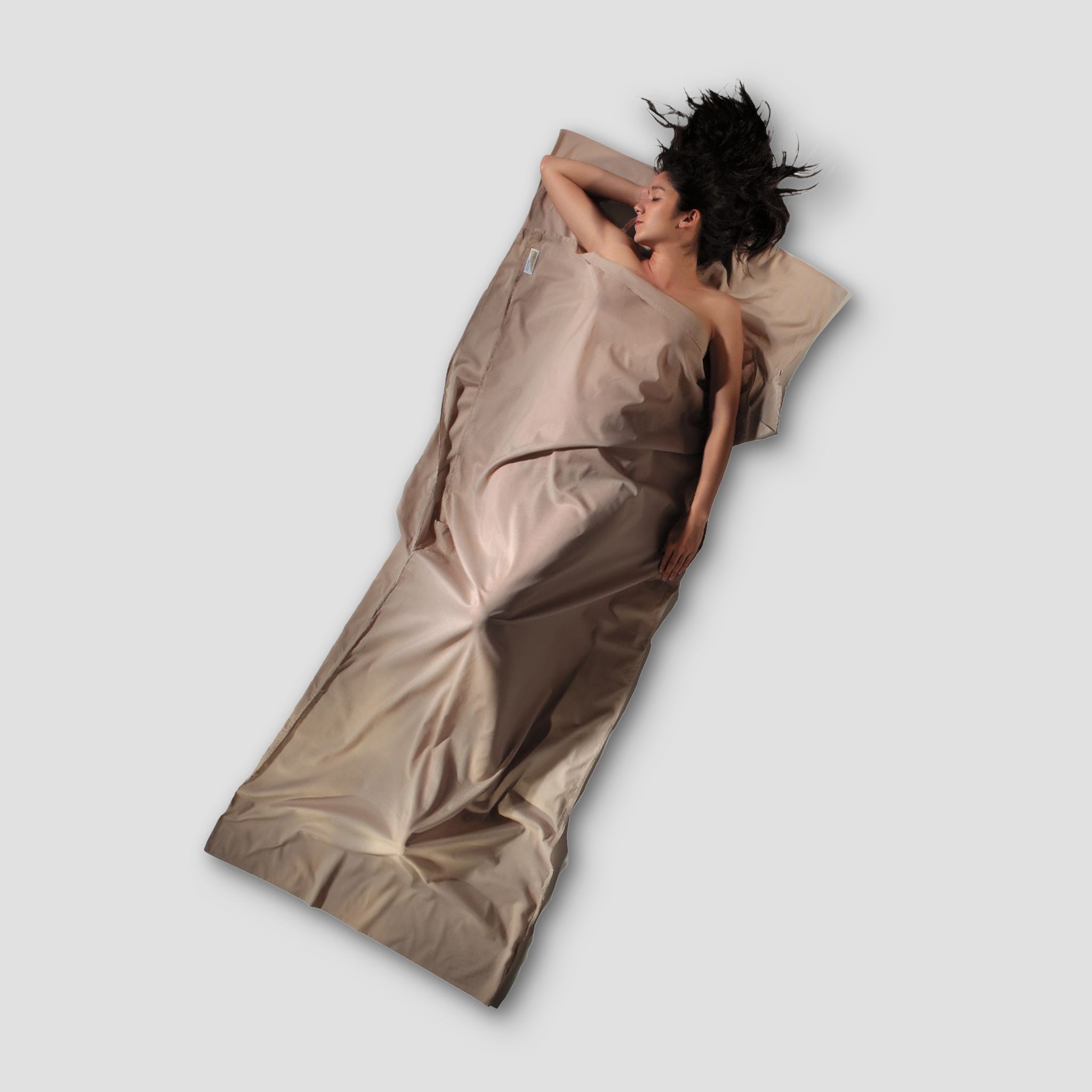 Person lying on a beige sleeping bag against a light gray background