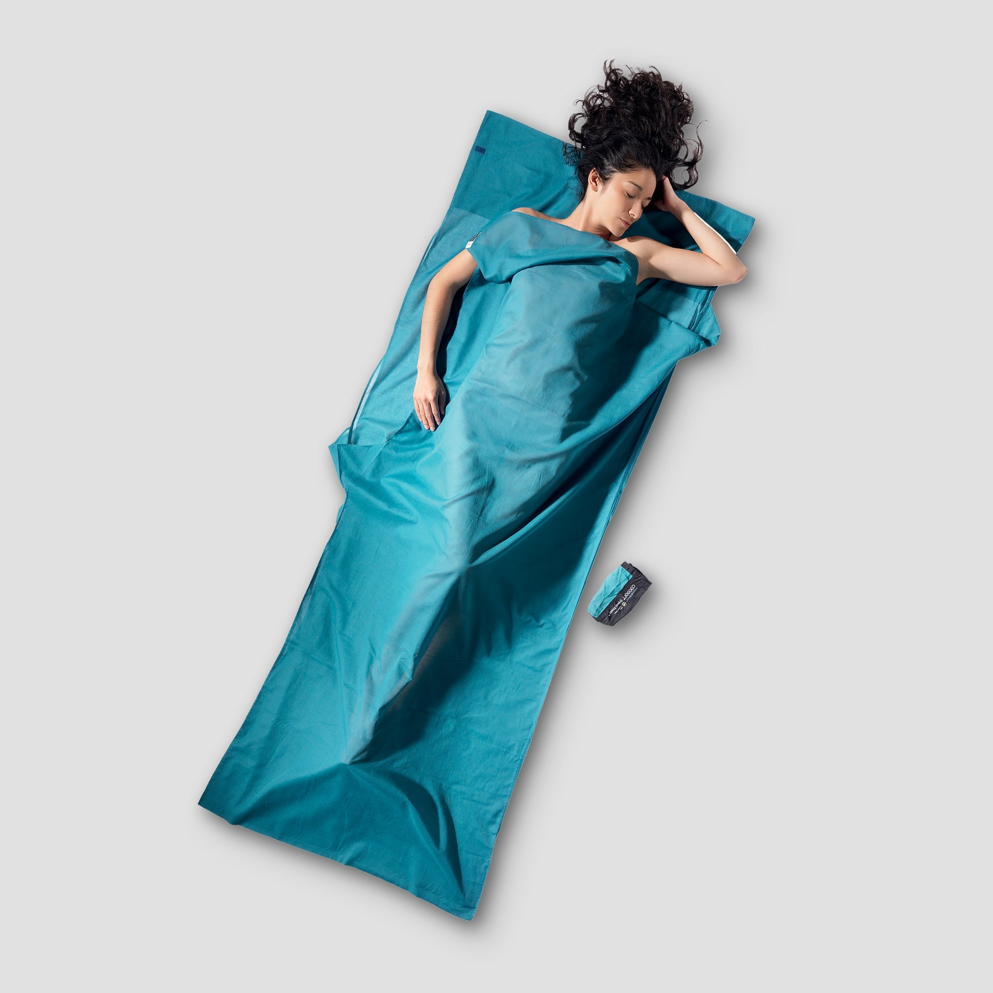 Person lying on a large blue mat with a small blue device next to them on a light gray background
