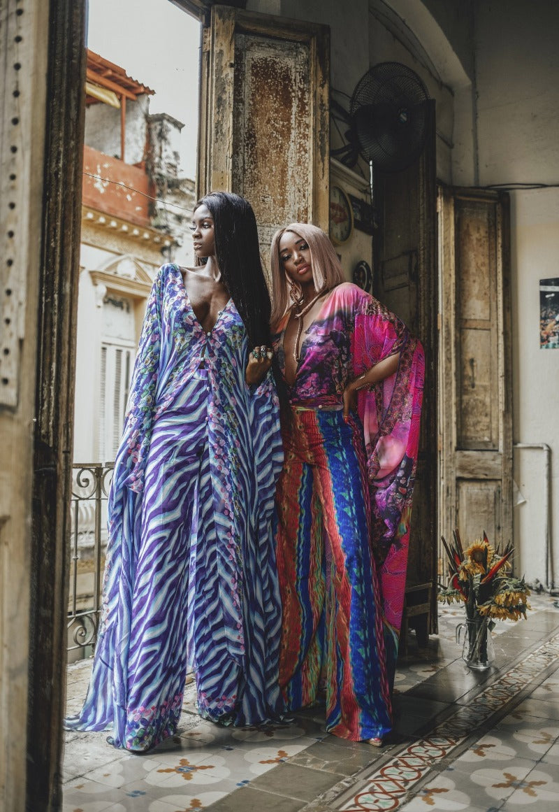 Two women in colorful patterned dresses standing in a doorway with decorative elements.