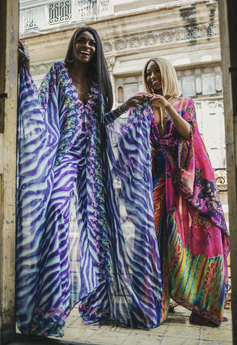 Two women wearing colorful, patterned dresses standing in front of a building.