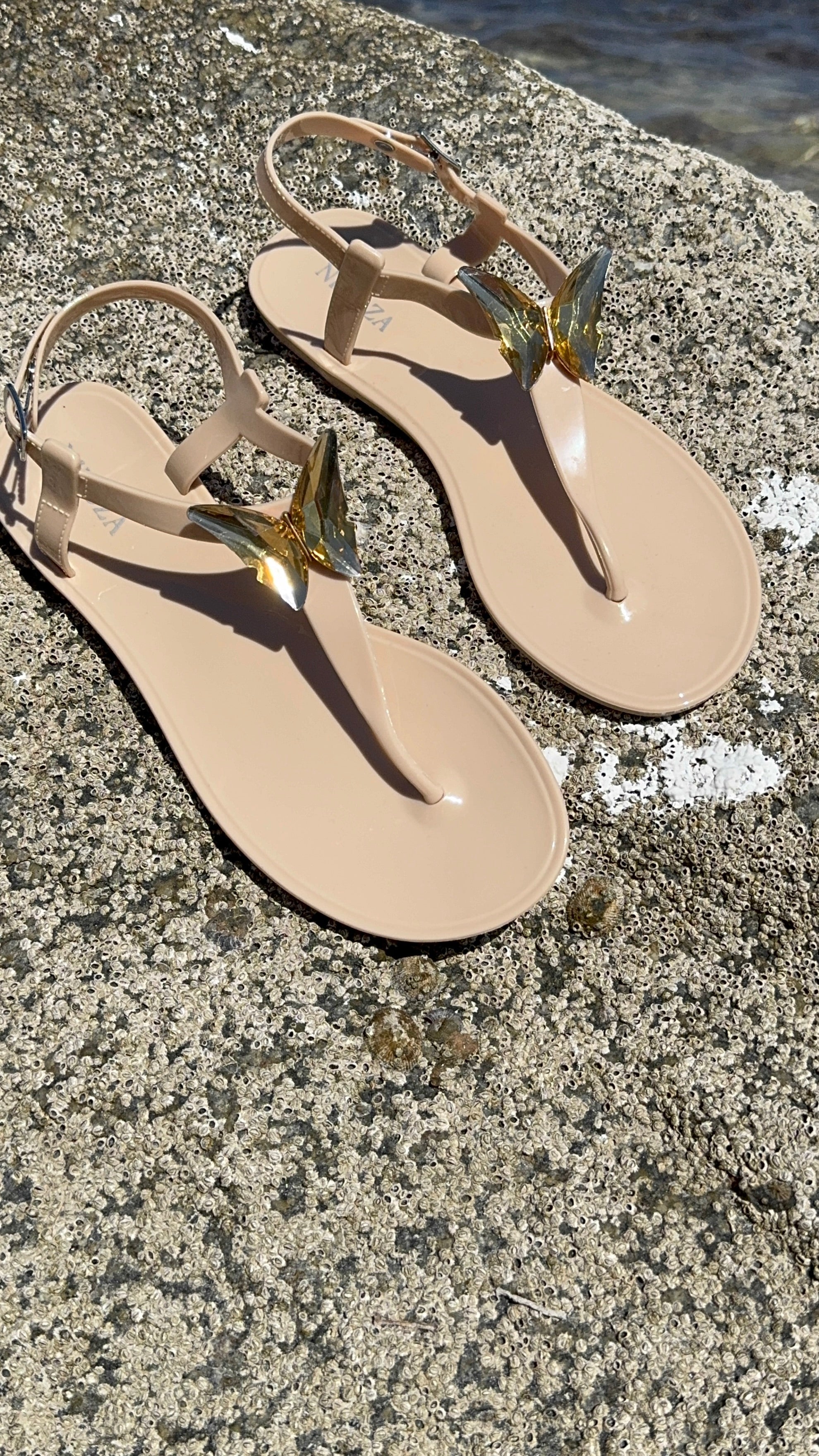 Beige sandals with gold straps on a textured surface near water