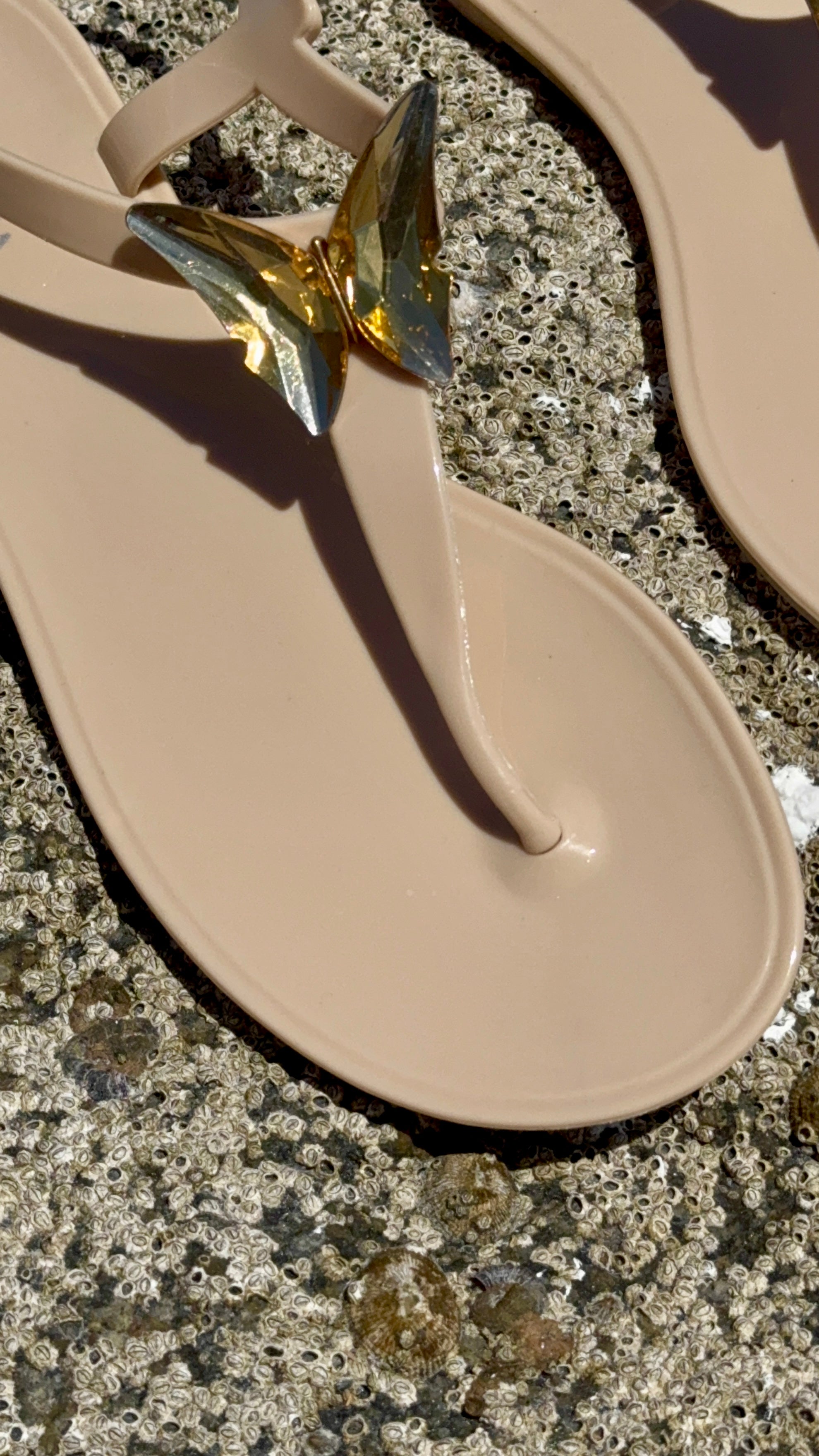 Beige sandal with a gold decorative element on a textured surface