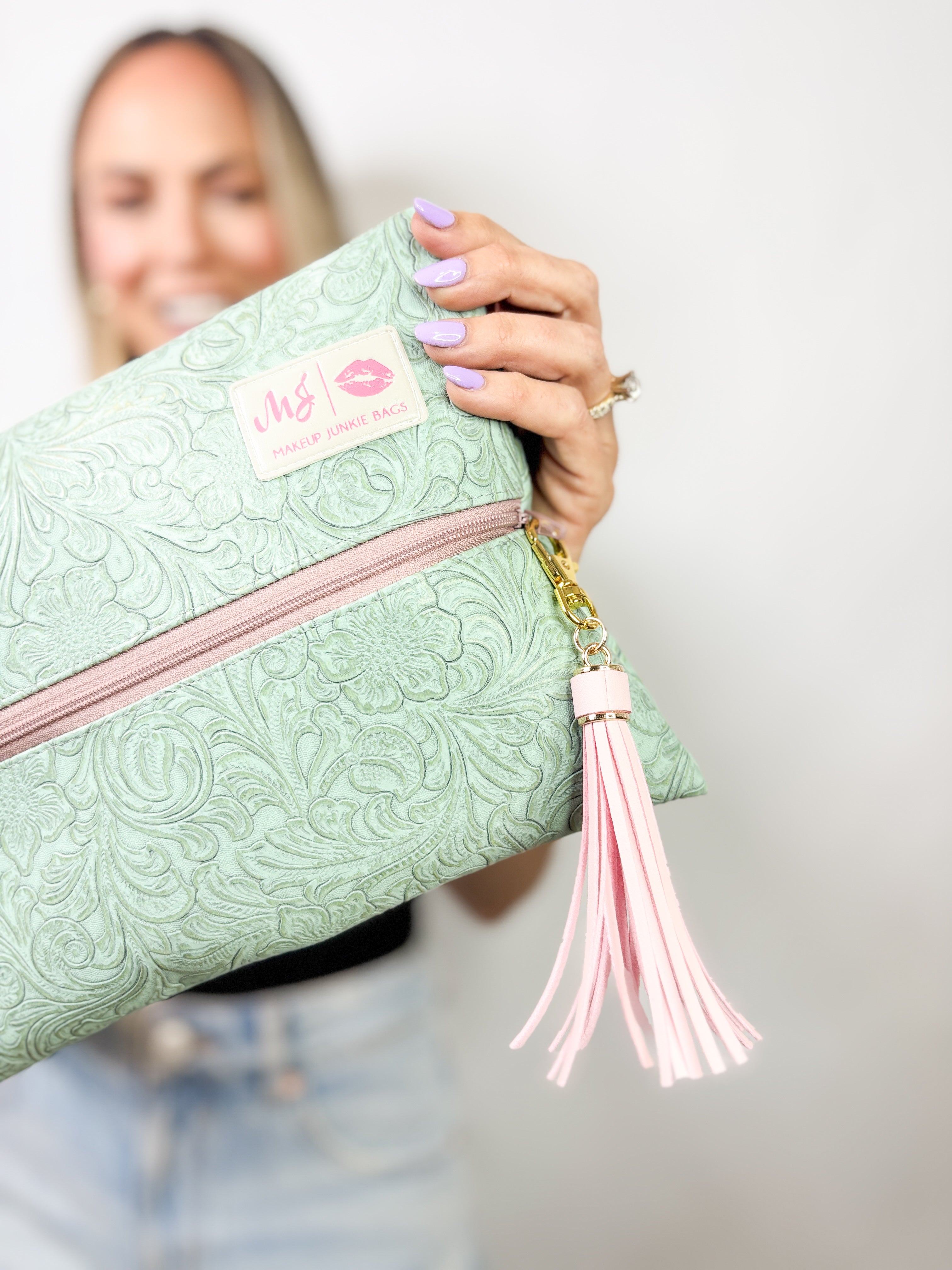 Mint green clutch with pink zipper and tassel held by a person against a neutral background