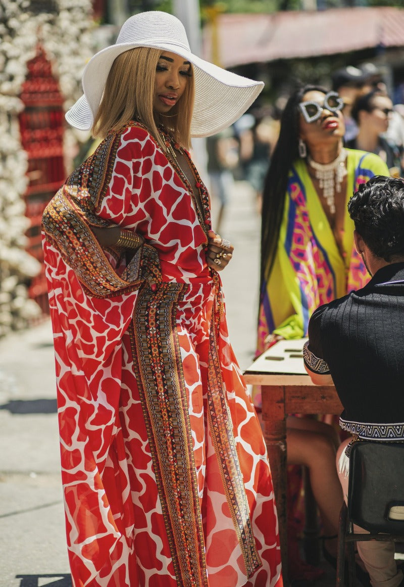 Woman in a red patterned dress and white hat interacting with others outdoors.