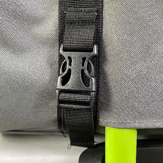 Close-up of a gray bag with a black strap and buckle, featuring a brand logo.