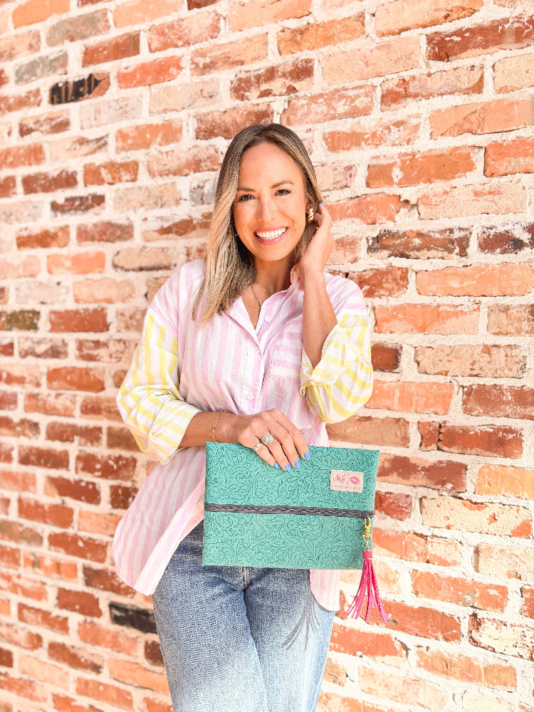 Woman holding a teal clutch with pink tassel against a brick wall