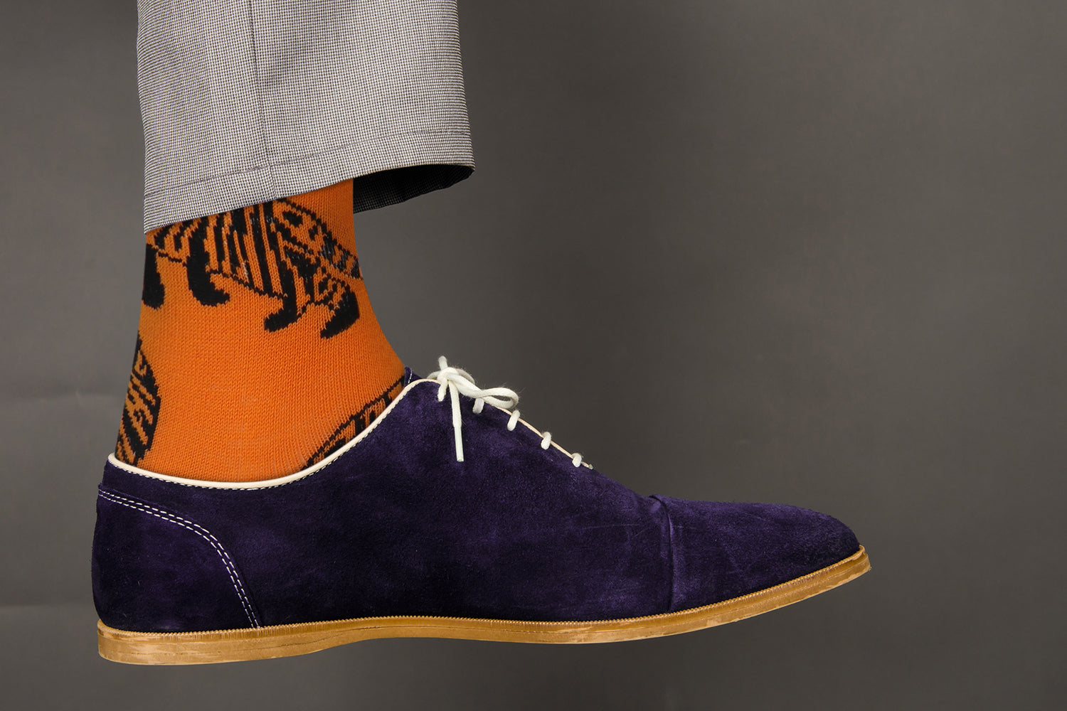 Navy suede shoe with orange and black tiger pattern sock on a gray background