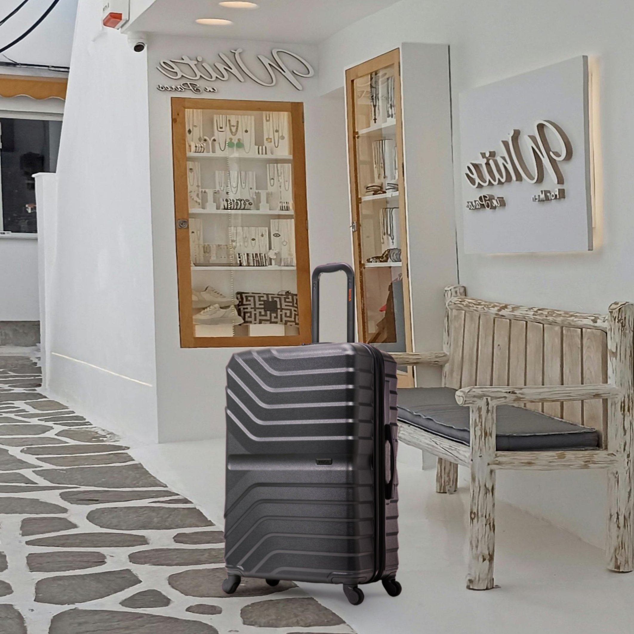 Gray suitcase on a stone-patterned floor with a wooden bench and decorative wall art in the background.