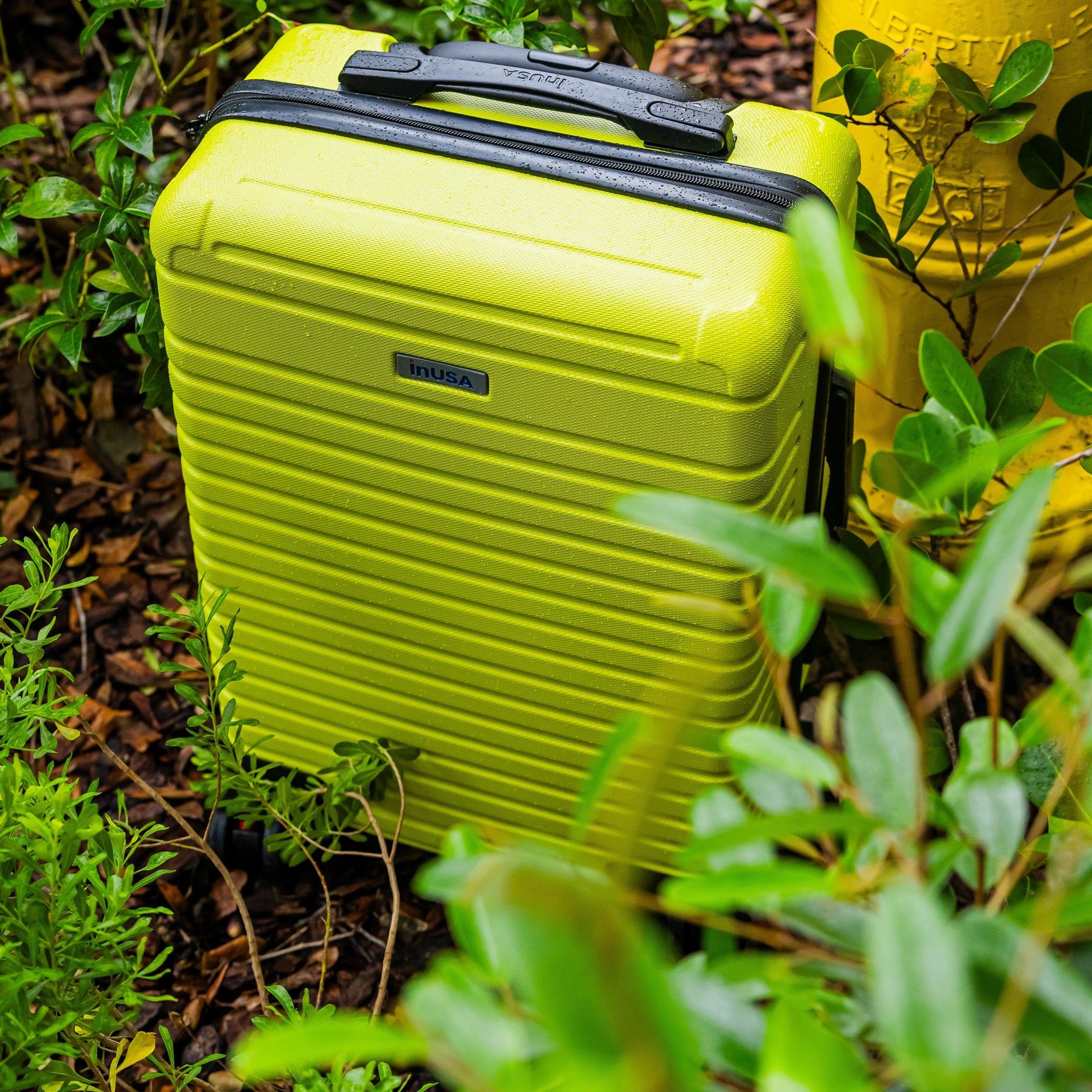 Yellow suitcase with black handle surrounded by green plants