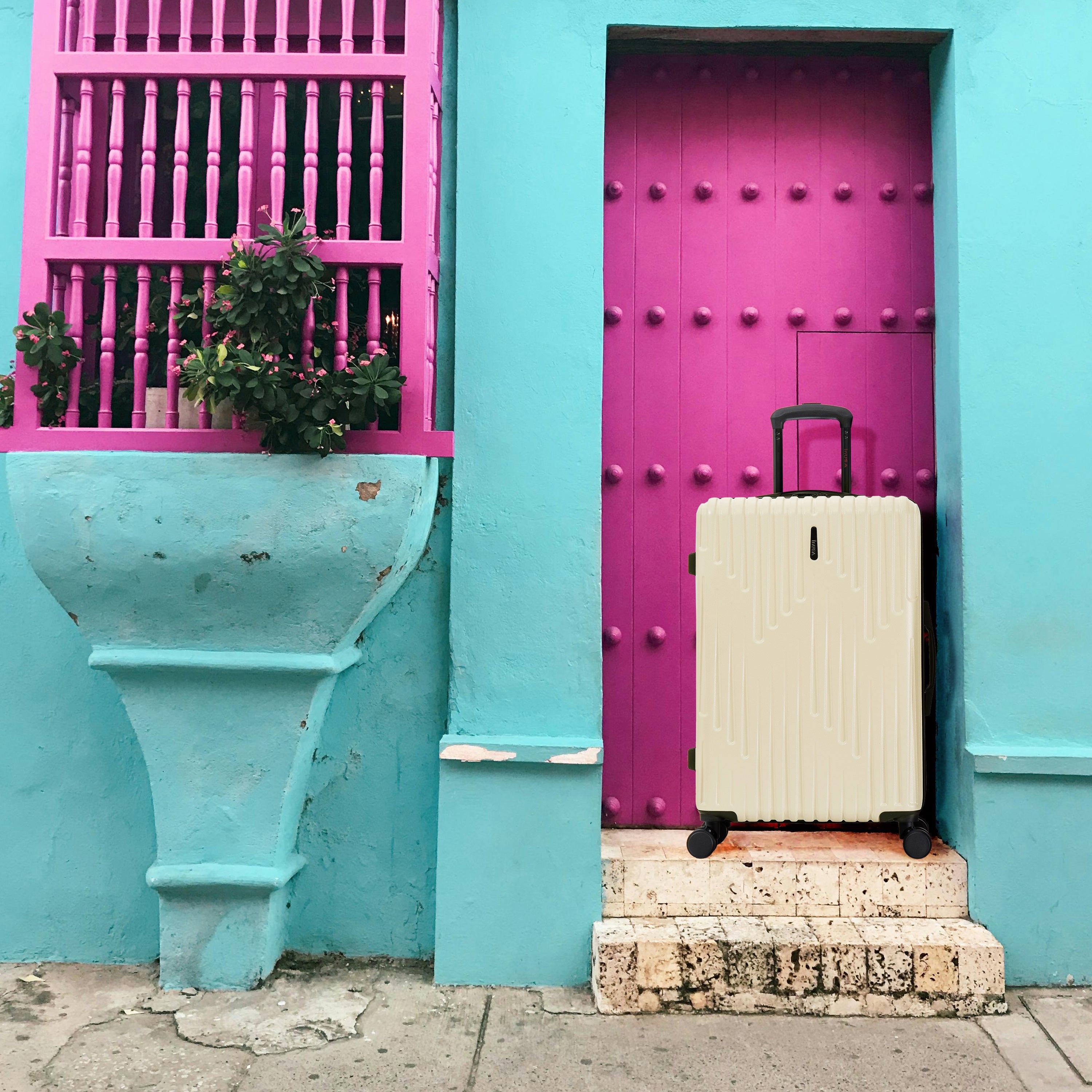 Beige suitcase on a stone step in front of a turquoise wall with a pink door.