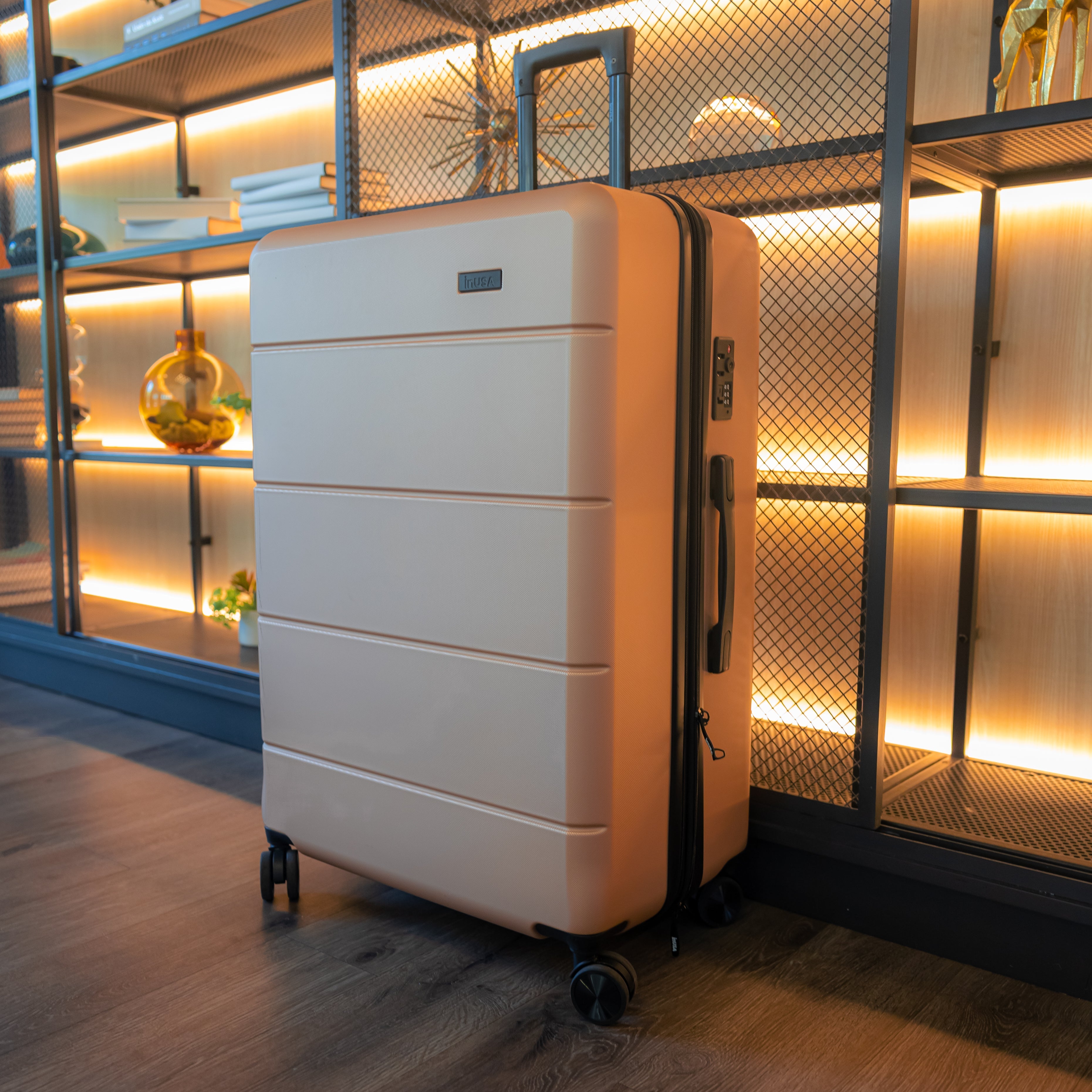 Beige suitcase on wheels in a room with wooden floor and decorative wall.