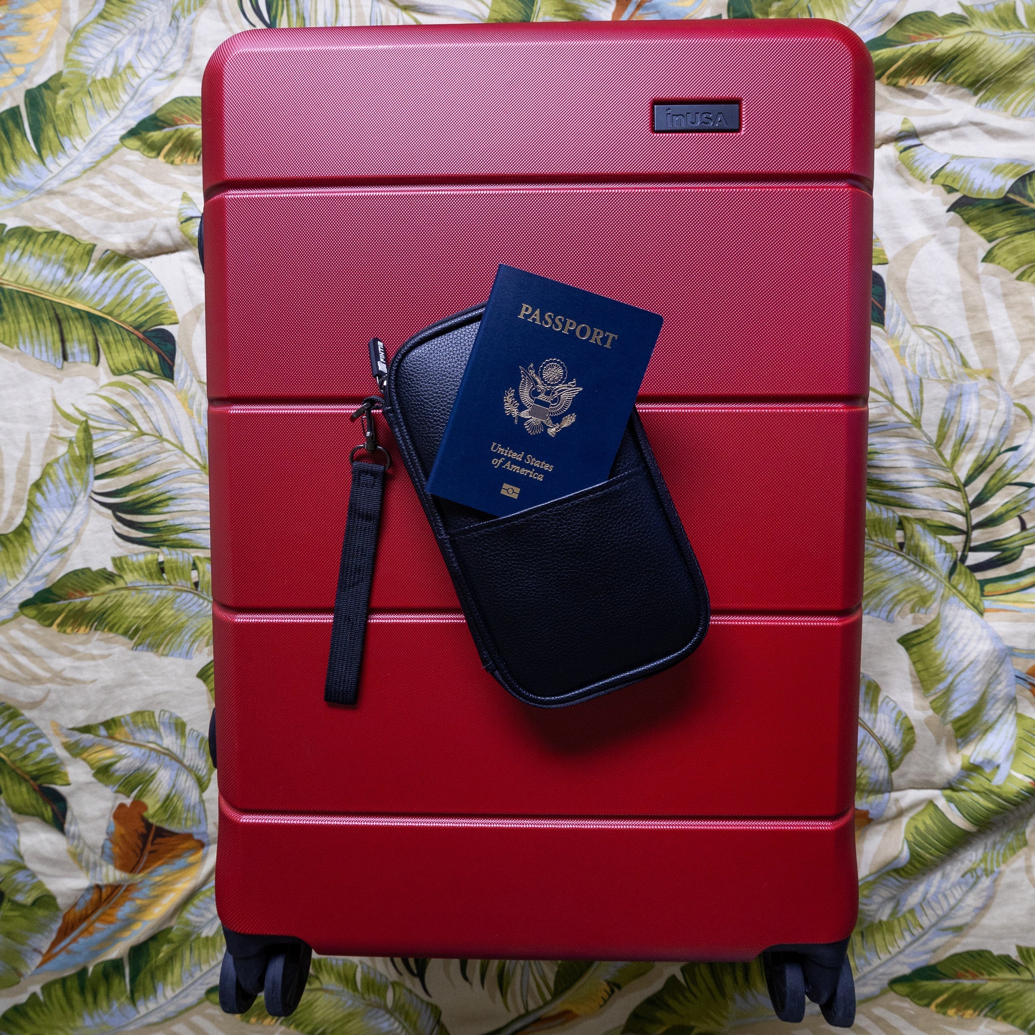 Red suitcase with a passport holder and passport on a floral-patterned surface
