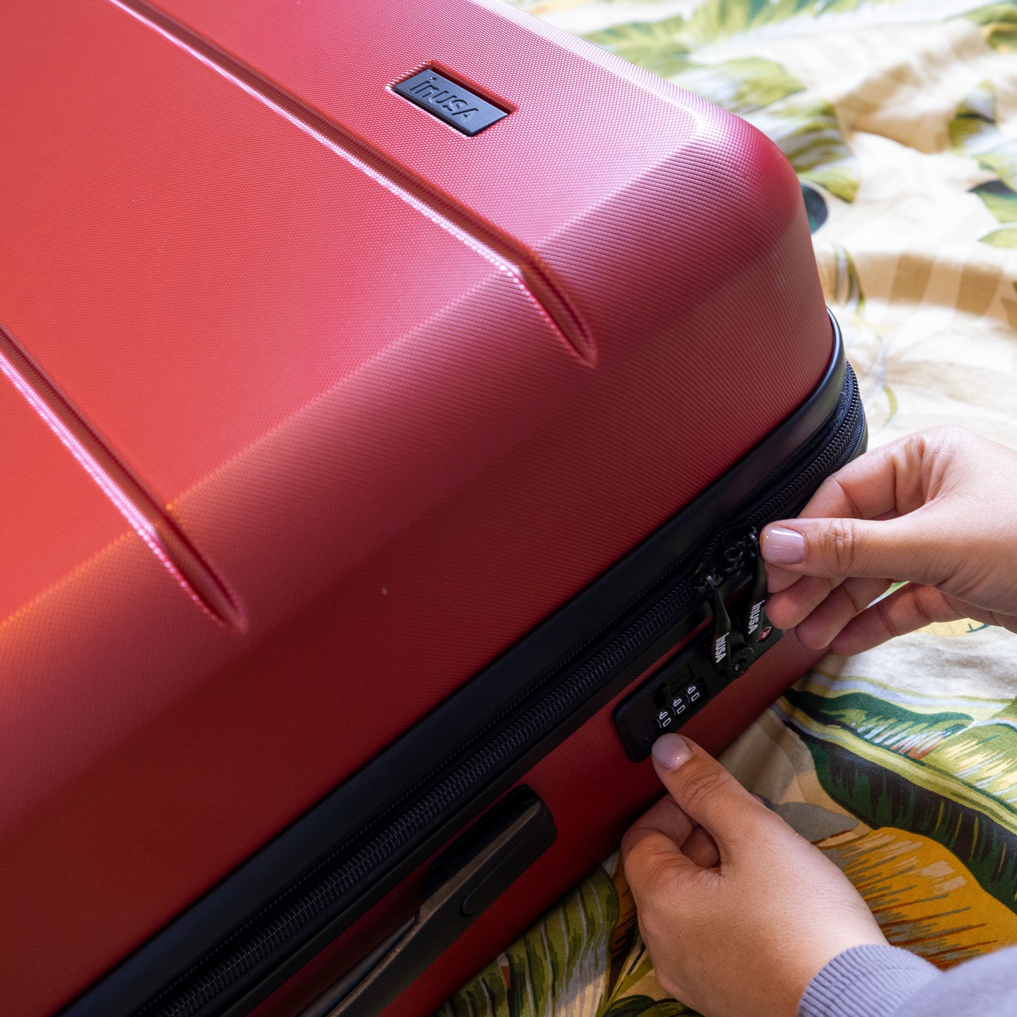 Red suitcase with a person's hand opening it on a colorful fabric background