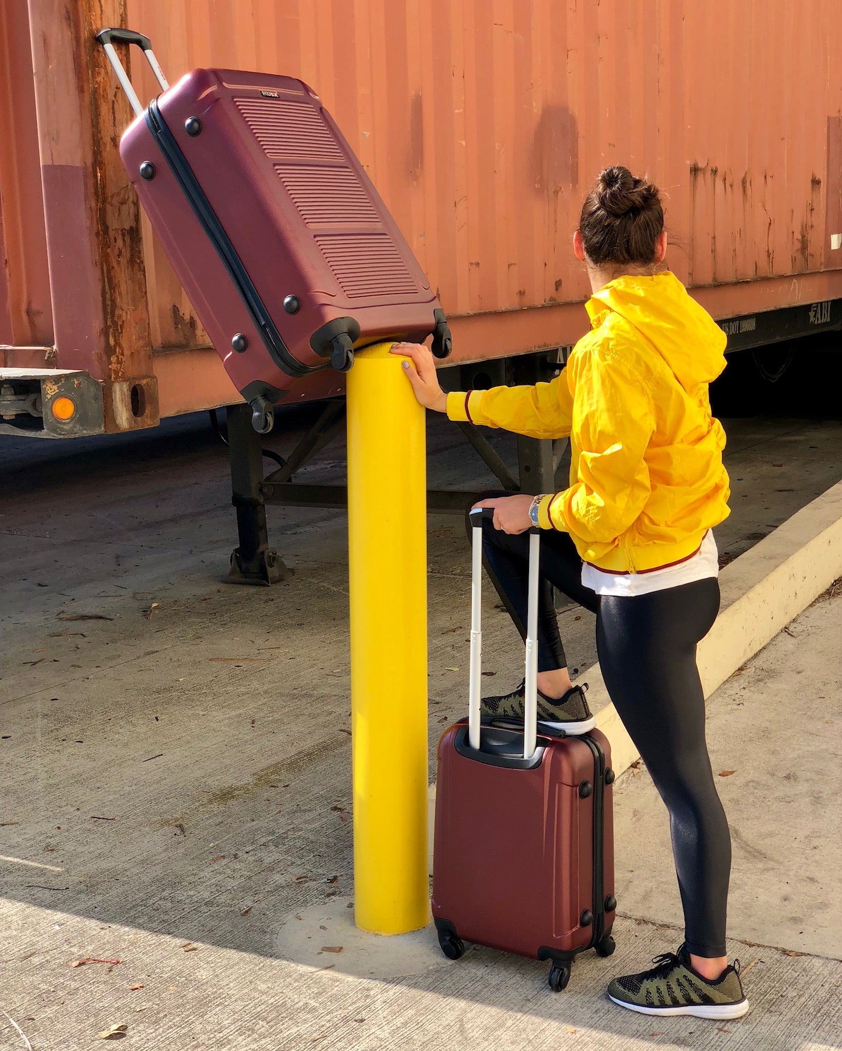 Person in yellow jacket with red suitcases near a yellow post on a train platform