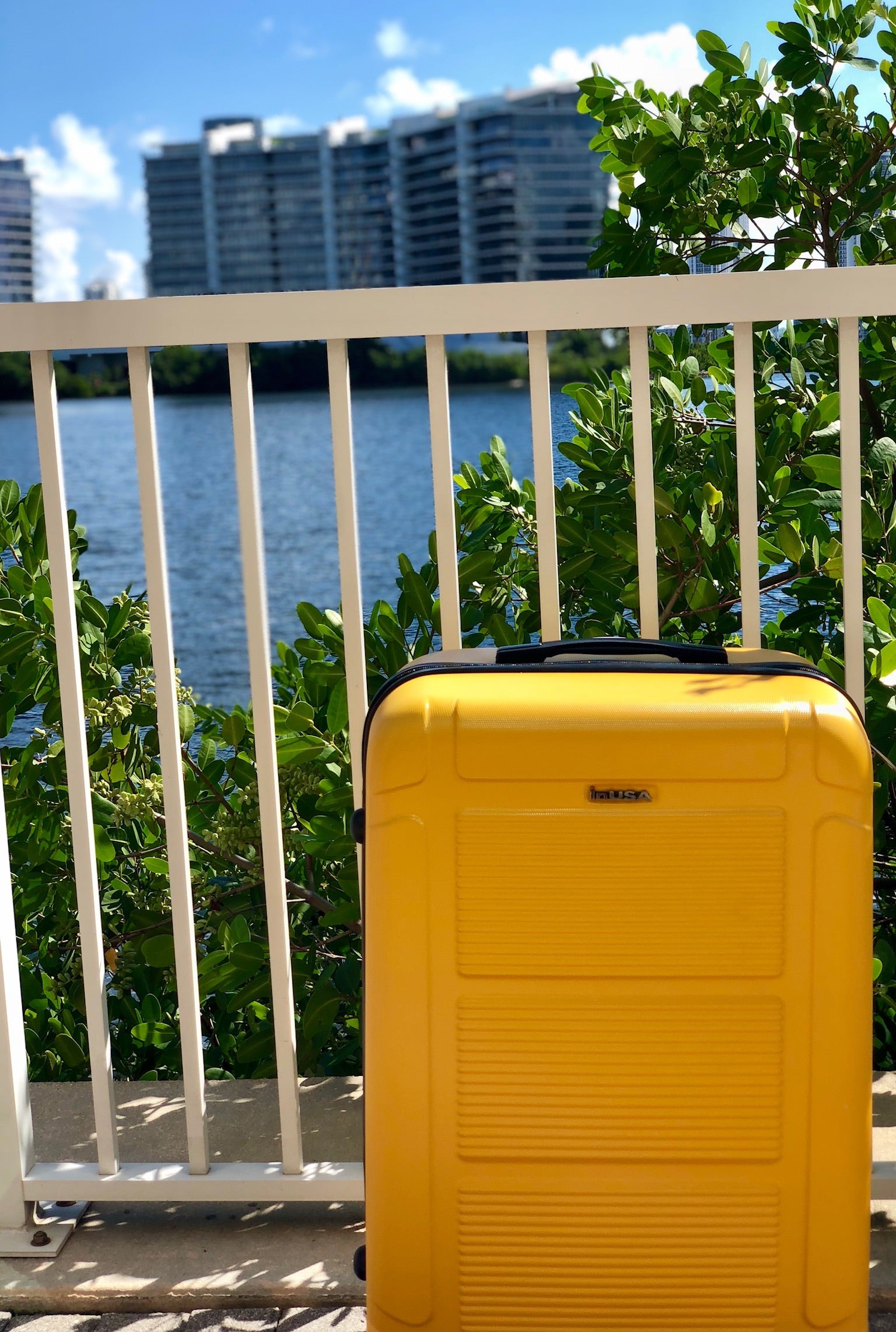 Yellow suitcase on a ledge with water and buildings in the background