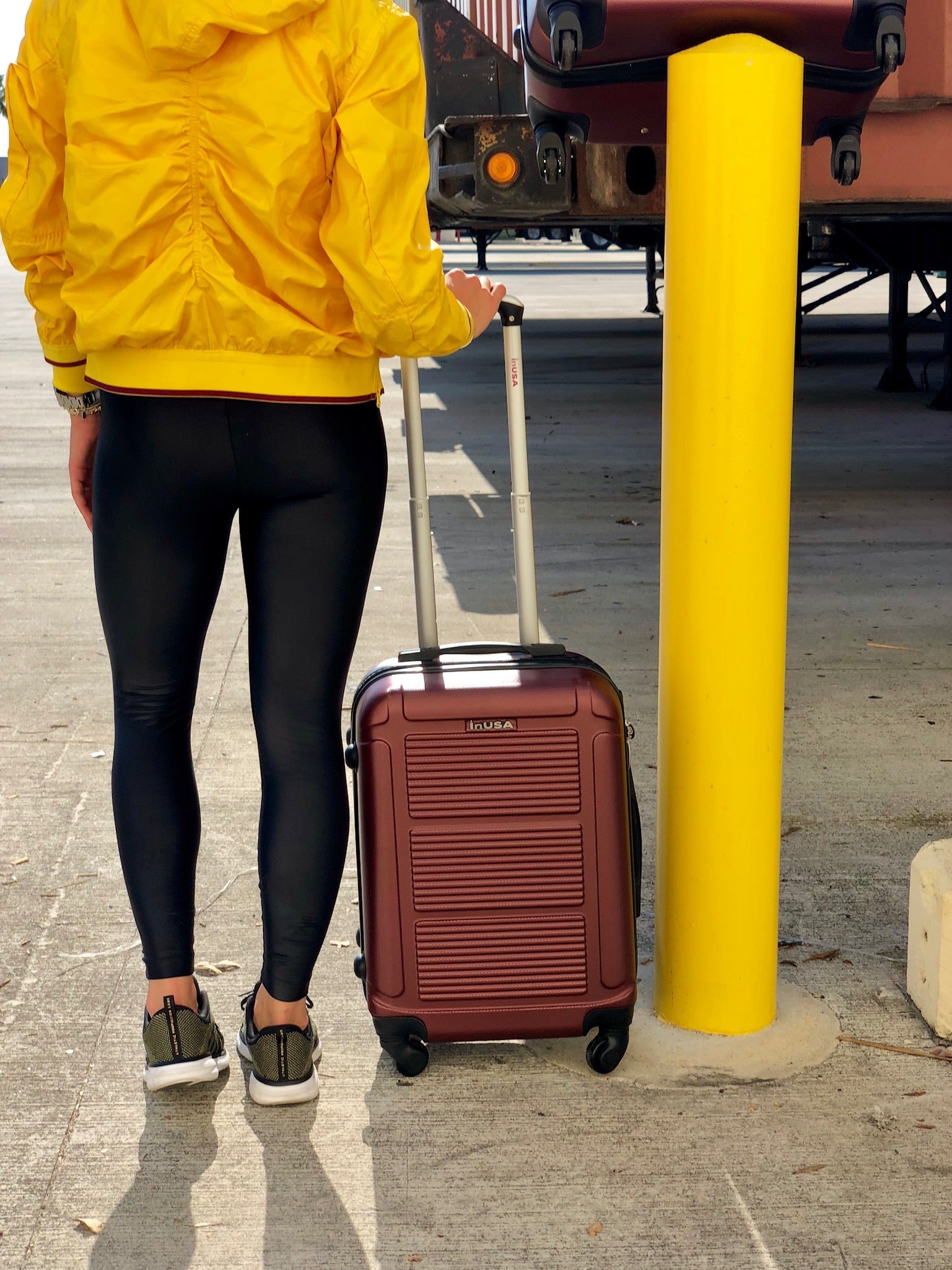 Person in yellow raincoat with a suitcase near a yellow post and train