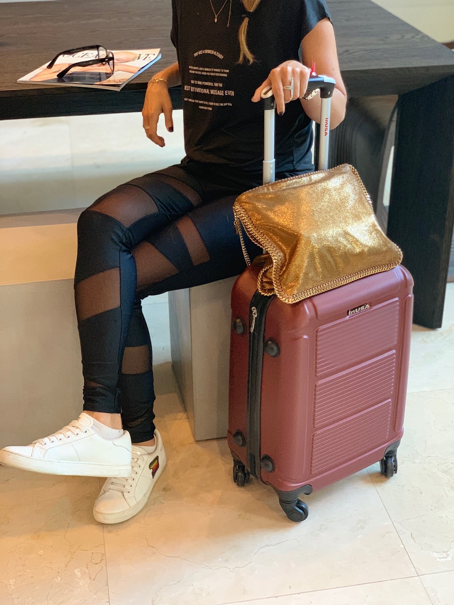 Person sitting with a suitcase and gold bag in an indoor setting