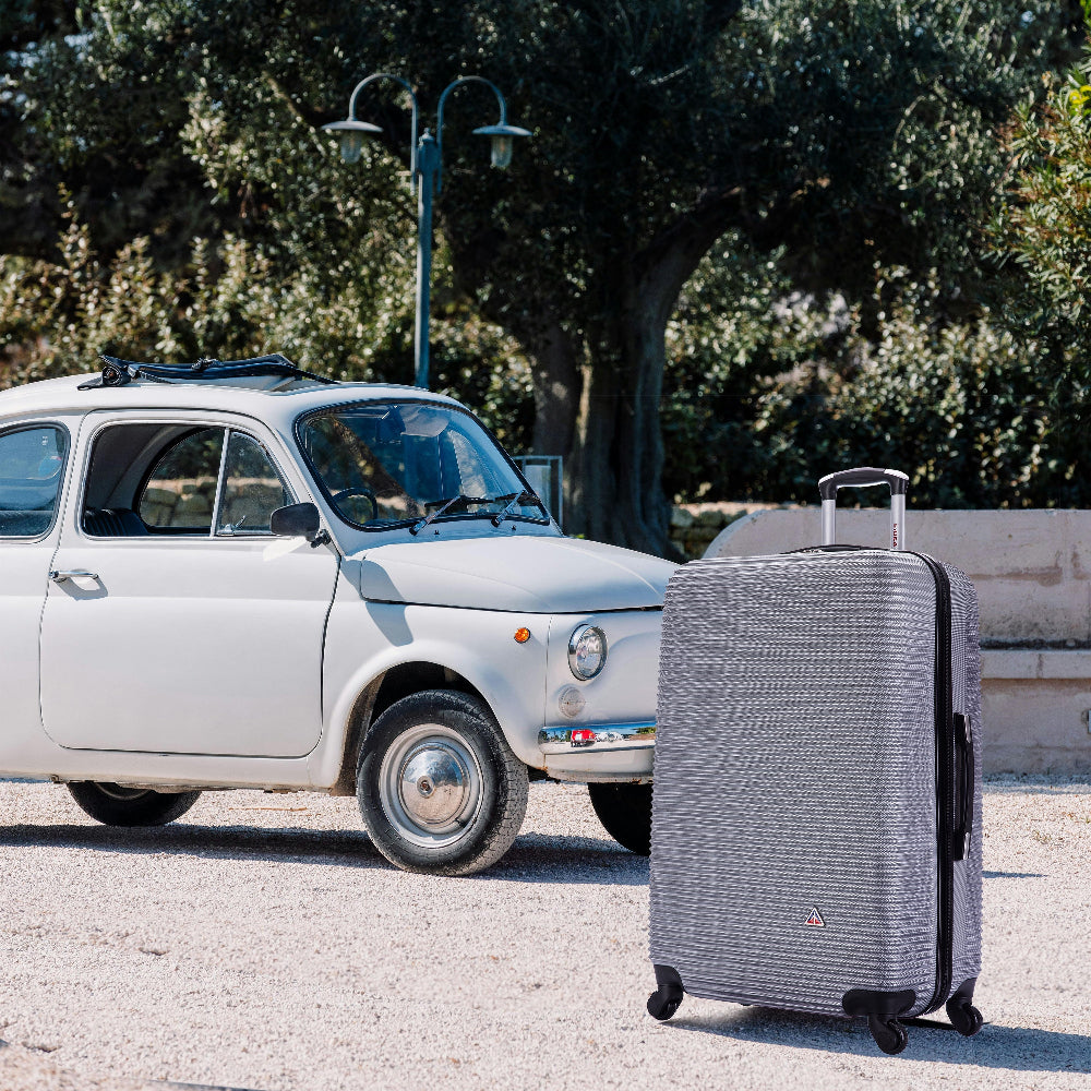Silver suitcase next to a white vintage car on a sunny day.