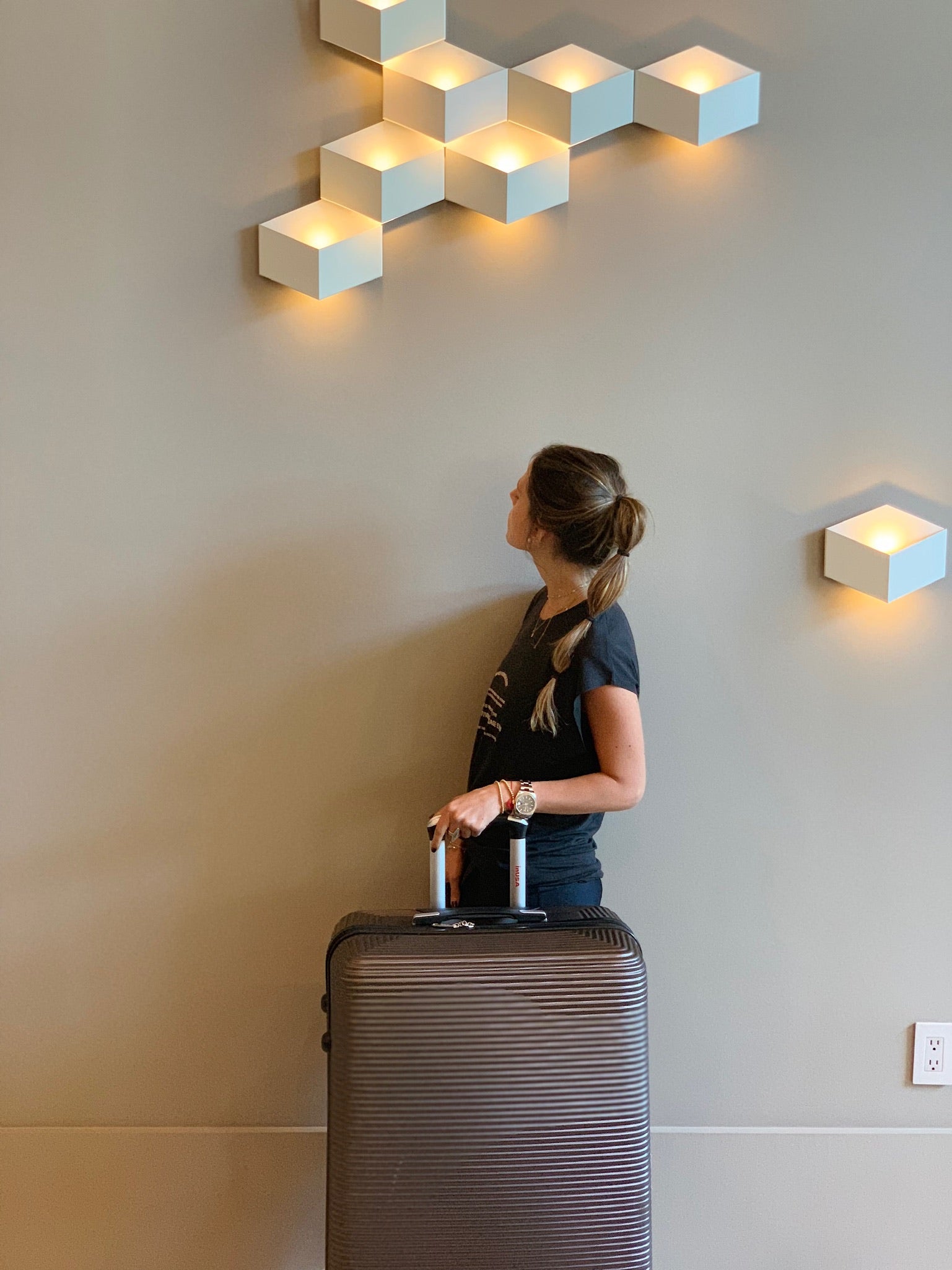 Woman with a suitcase in a room with geometric wall lights