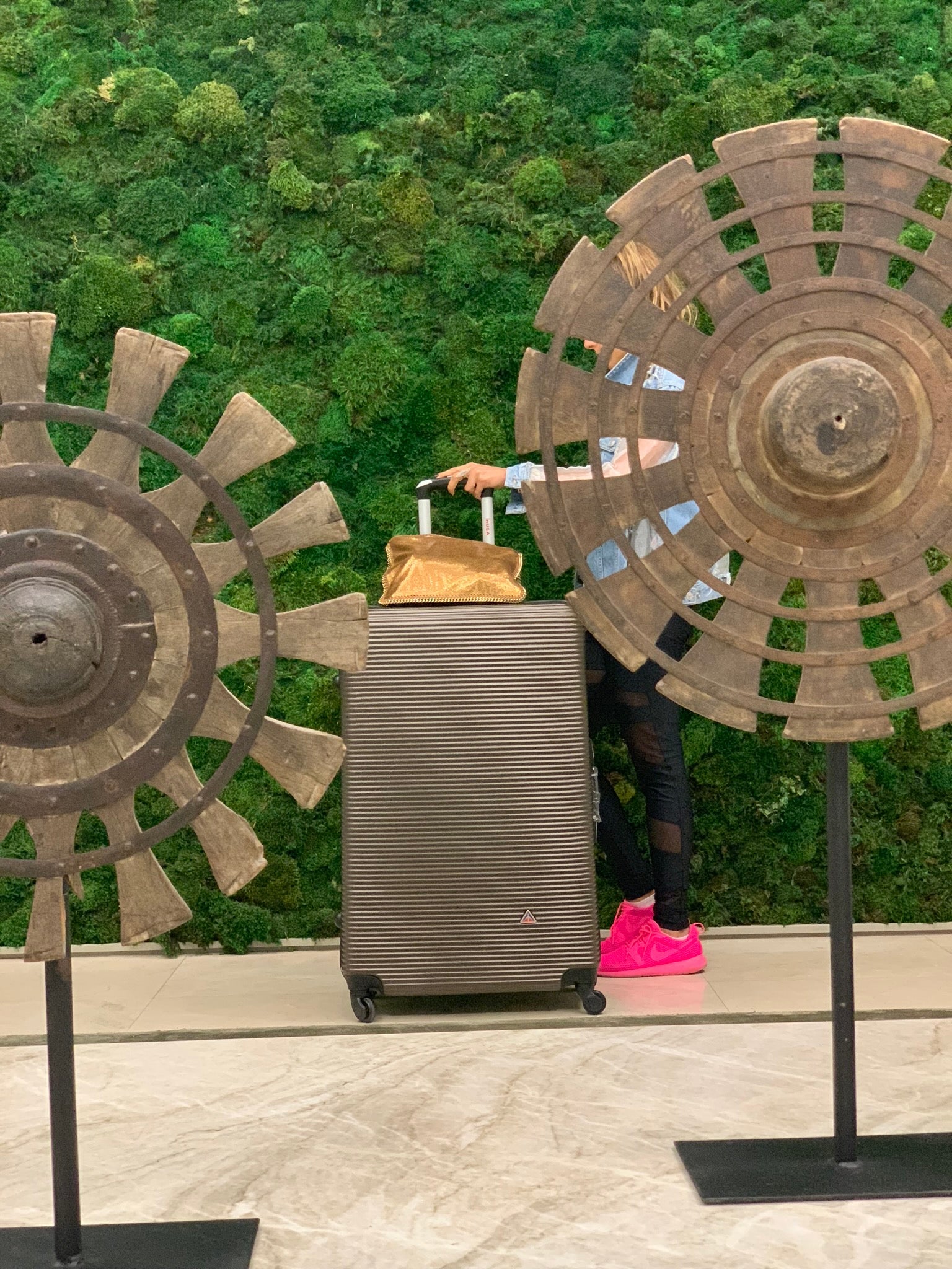 Person with a suitcase between two large decorative fans against a green wall.
