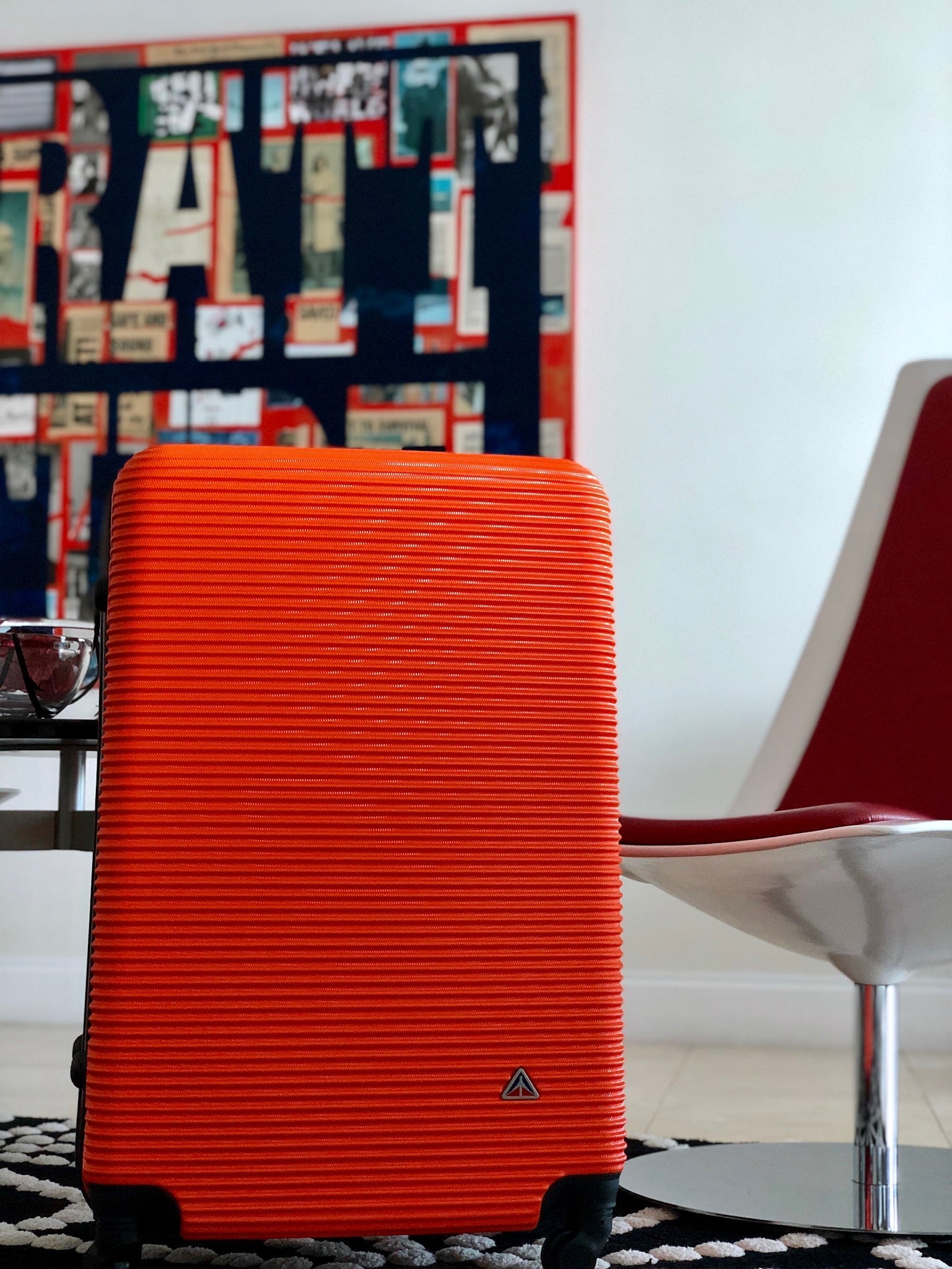 Orange suitcase on a rug with a colorful abstract painting in the background