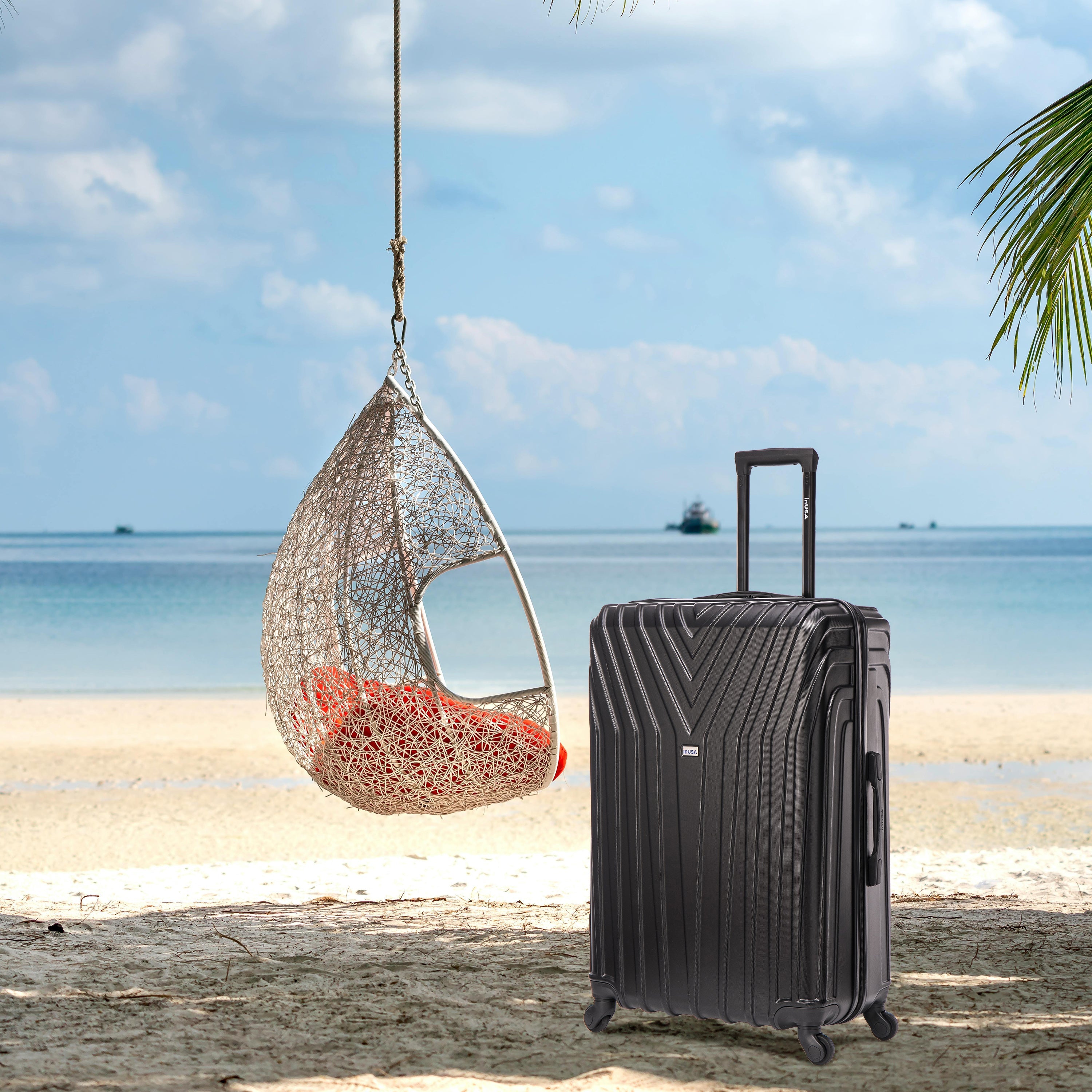 Black suitcase on a sandy beach with a hanging chair and ocean view