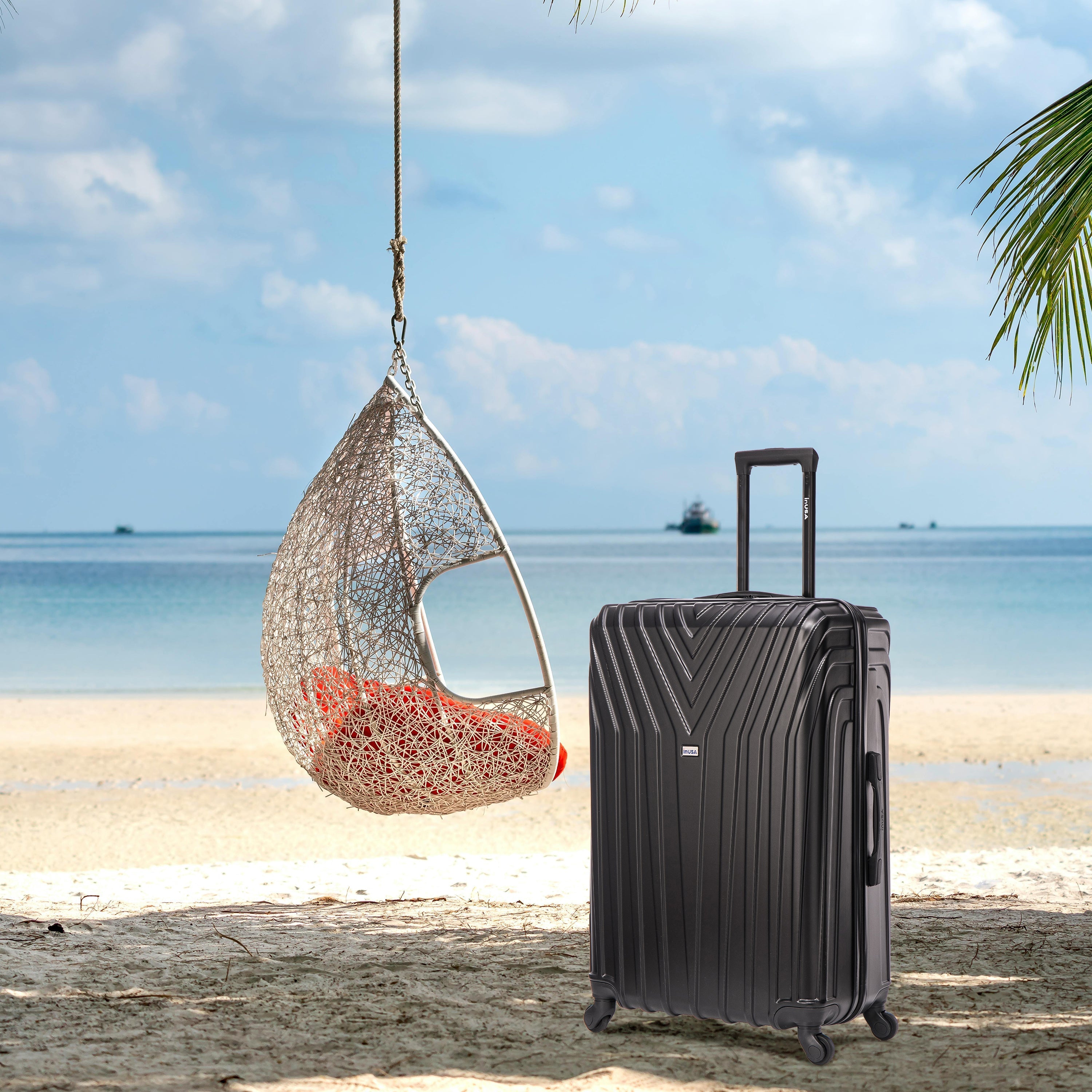 Black suitcase on a sandy beach with a hanging chair and ocean view
