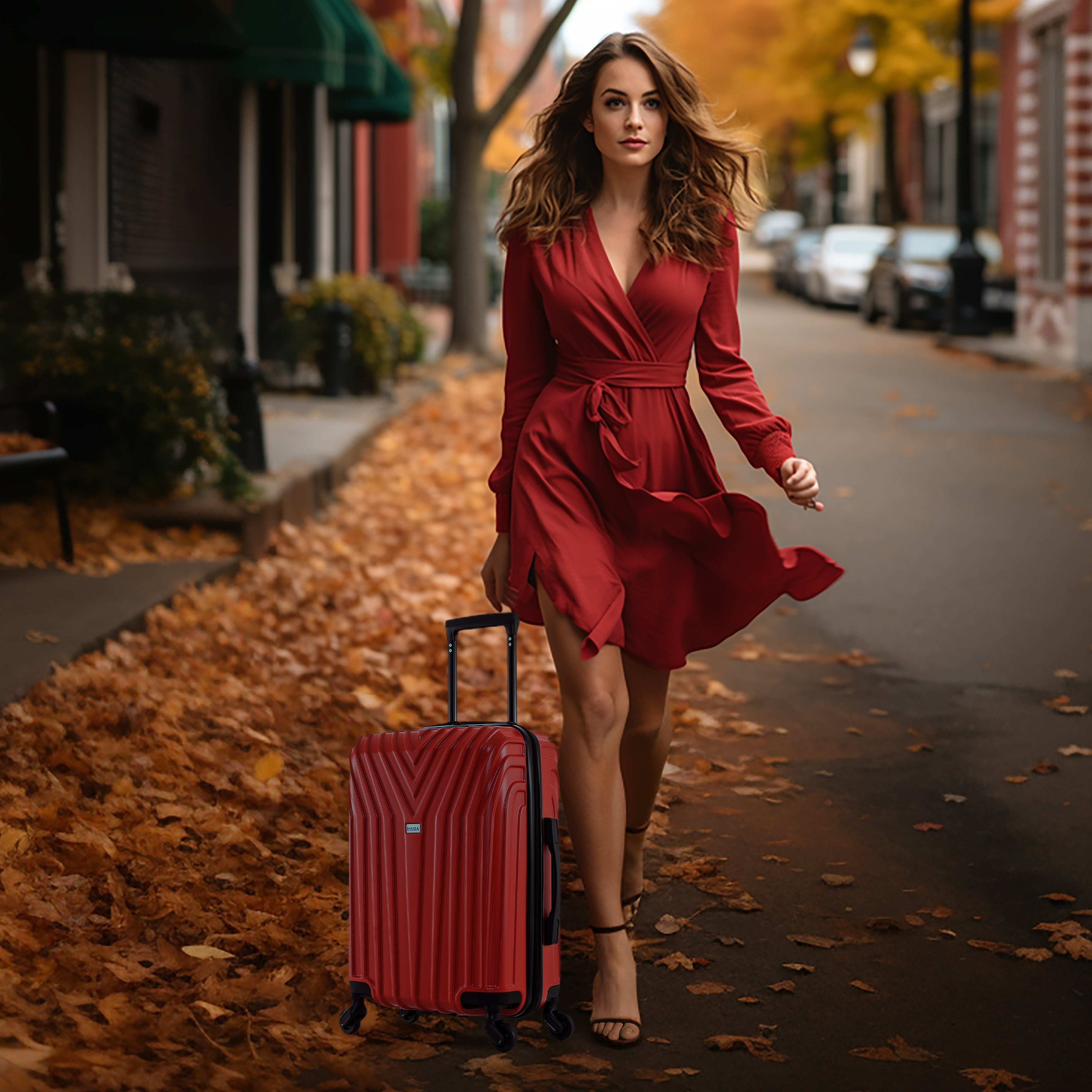 Woman in a red dress walking with a red suitcase on a street with autumn leaves.