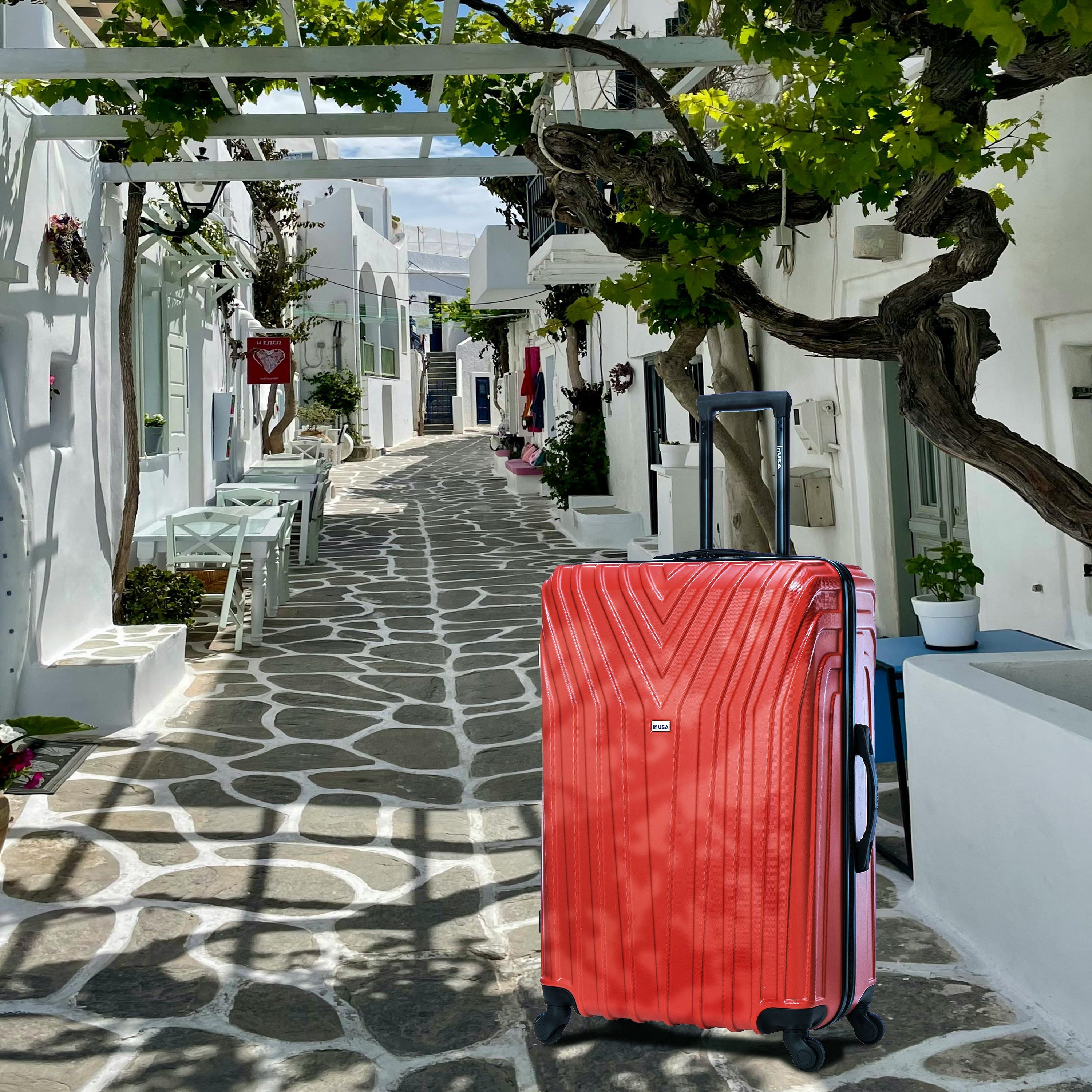 Red suitcase on a stone path with white buildings and greenery in the background