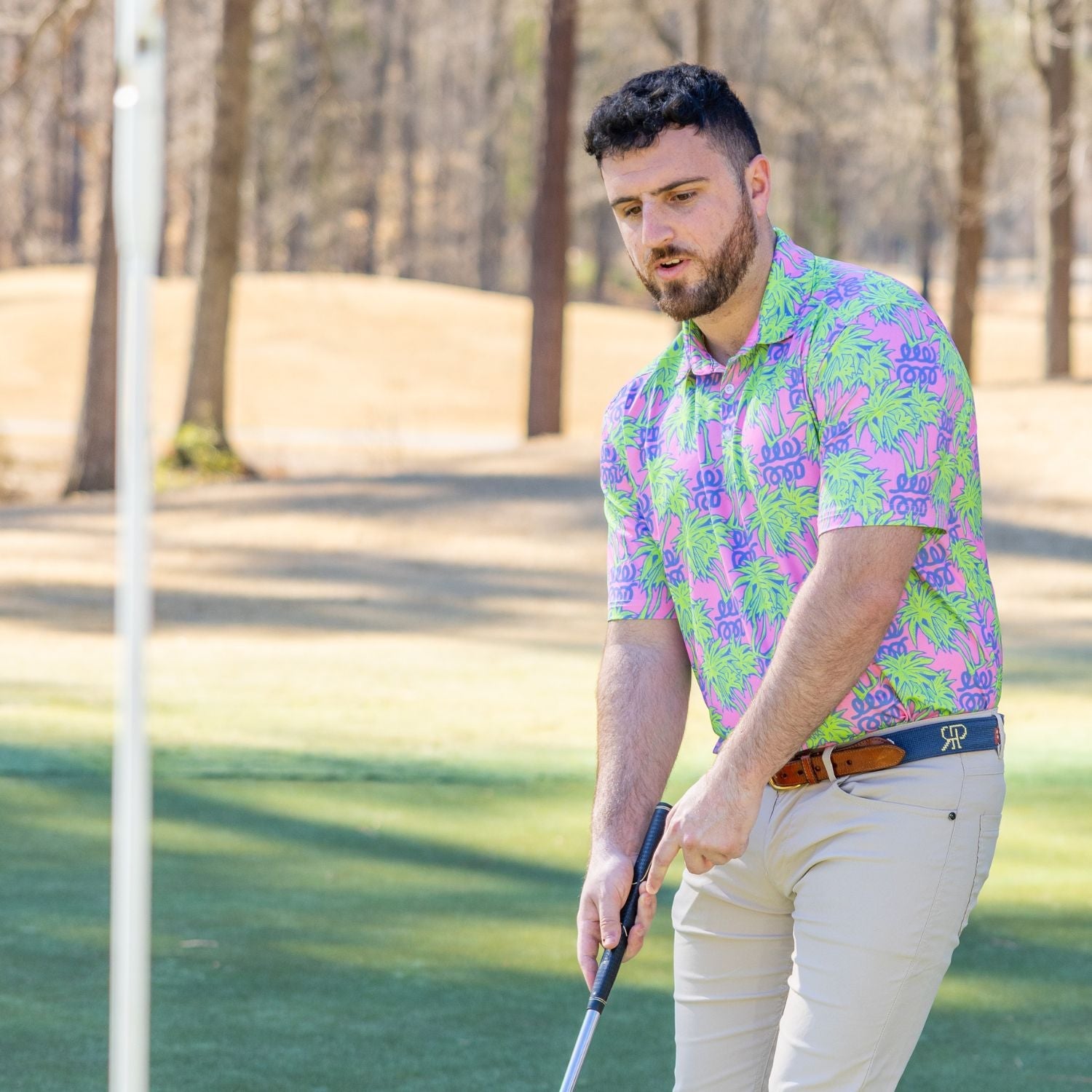 Man in a colorful shirt playing golf on a course with trees in the background