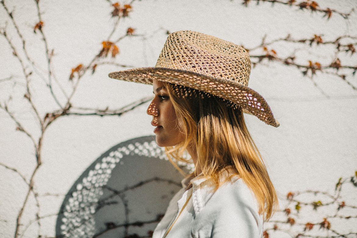 Woman wearing a straw hat against a neutral background with branches.
