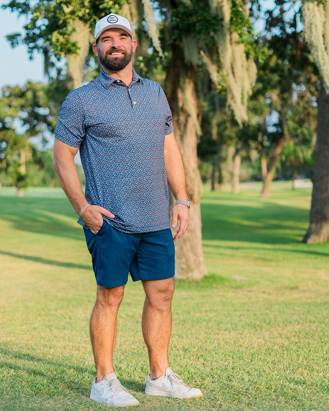 Man in golf attire standing on a golf course with trees in the background